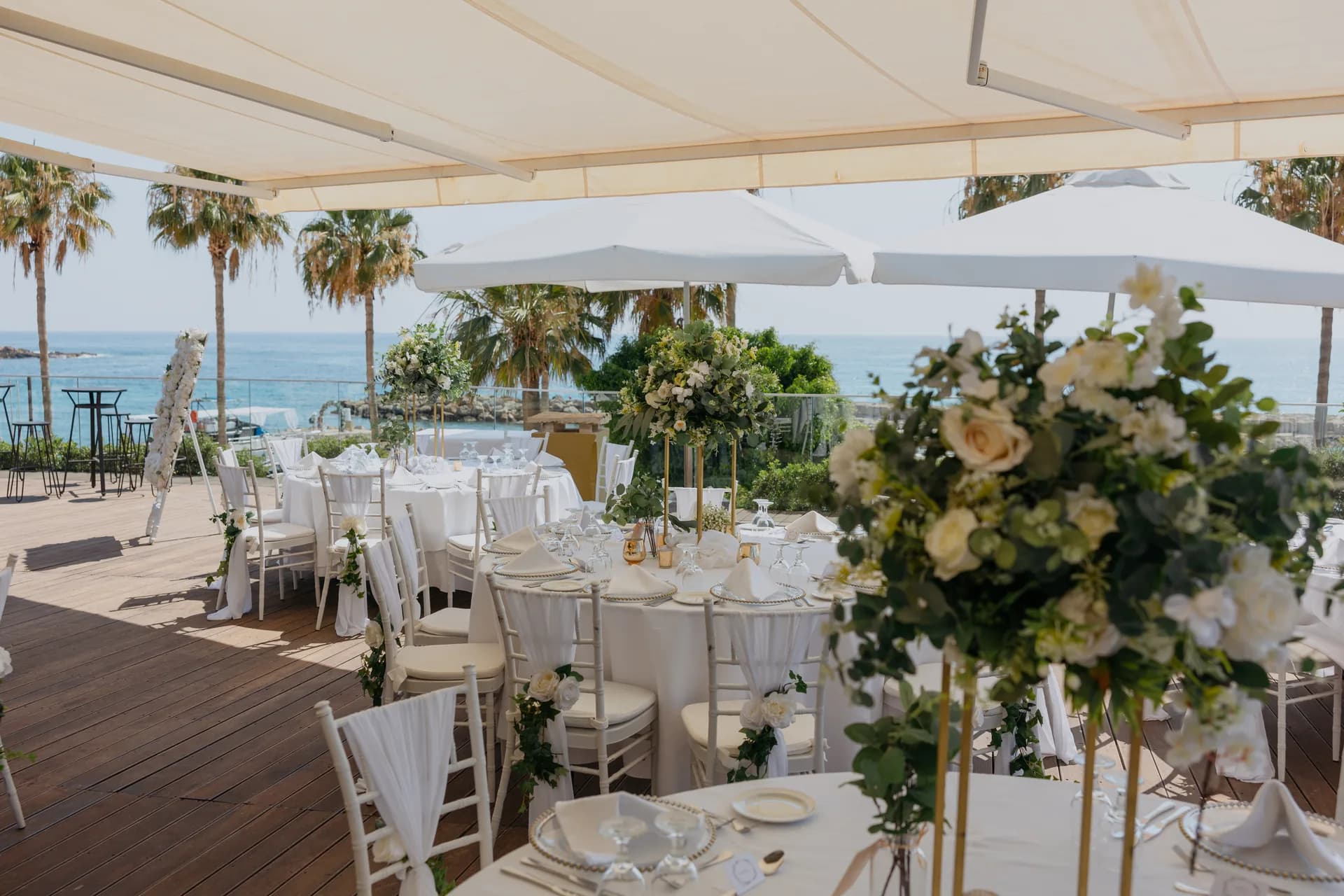 Dressed dining tables under the terrace awning at Coral Beach with palms and the open sea behind