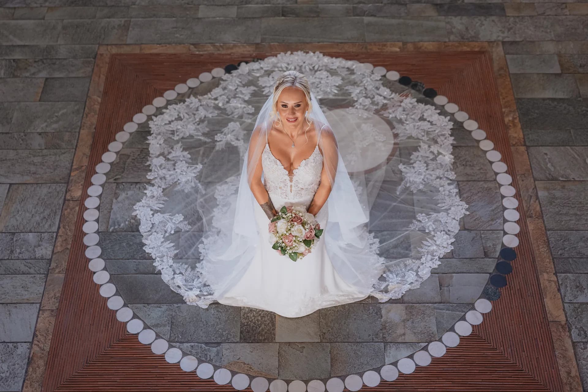 Overhead view of a bride, veil spread, standing inside a circular stone inlay at Coral Beach