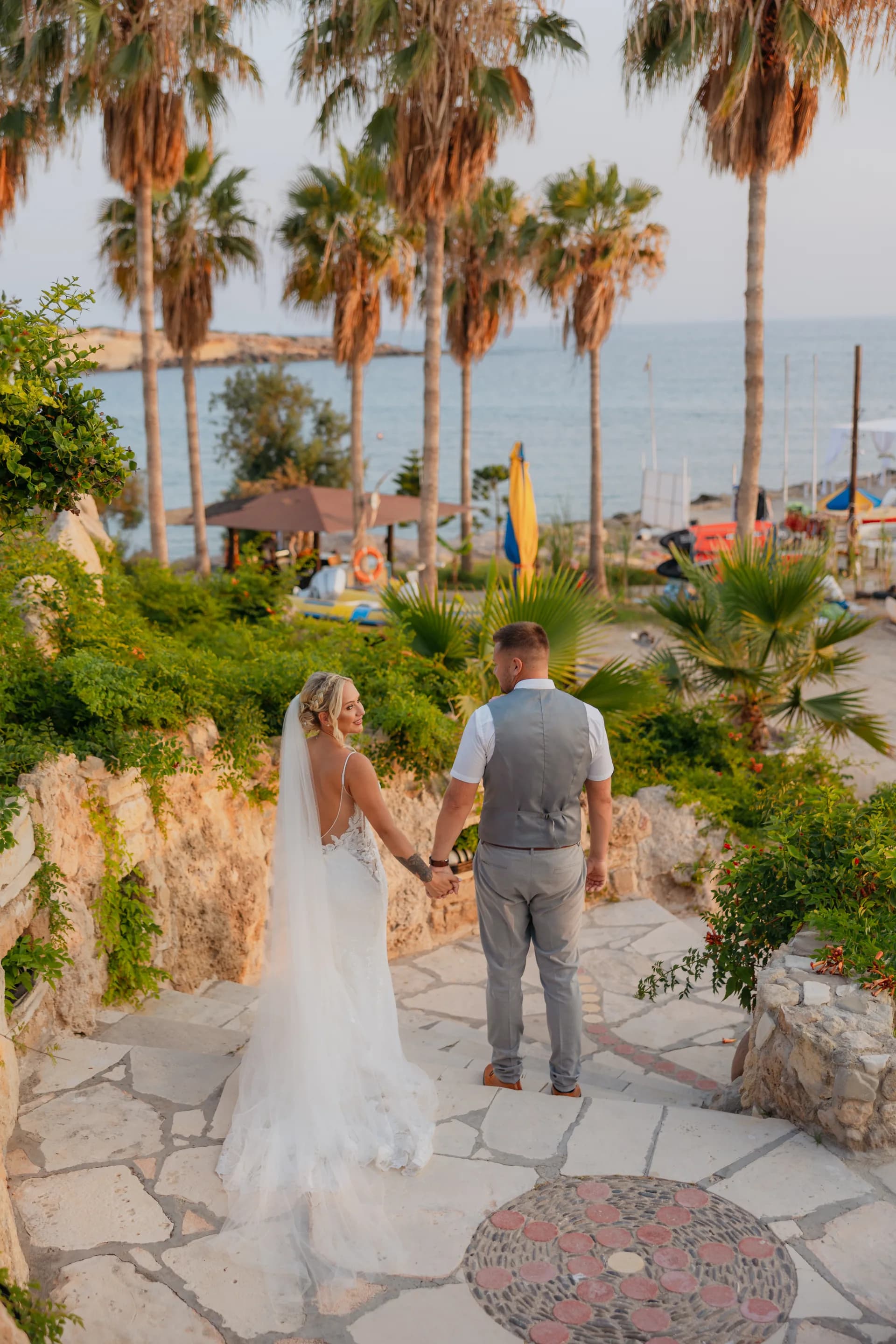 Couple walking a palm-lined stone path down through the gardens at Coral Beach towards Coral Bay