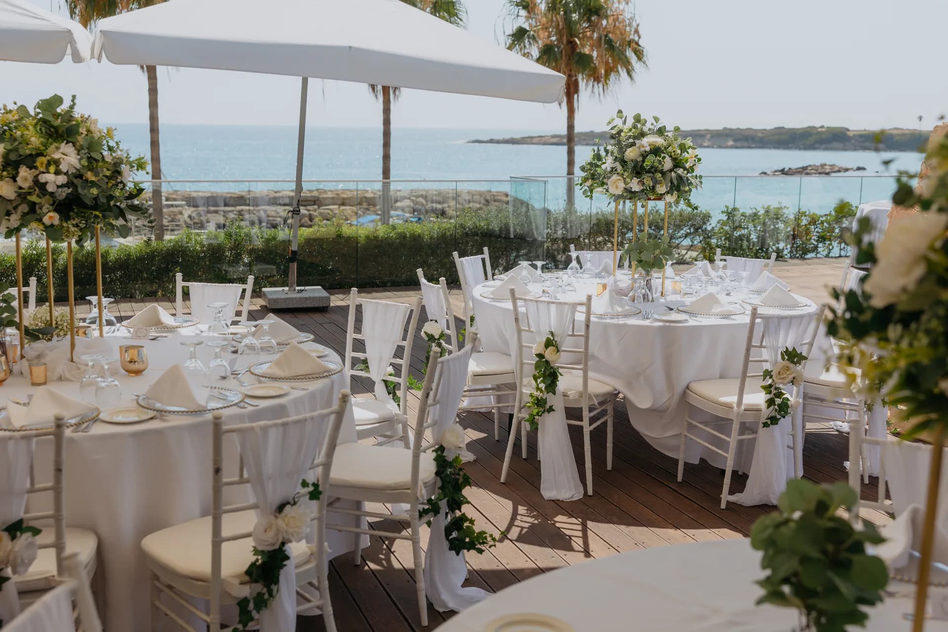 Round reception tables with chiavari chairs and tall floral centrepieces on the sea-view terrace at Coral Beach