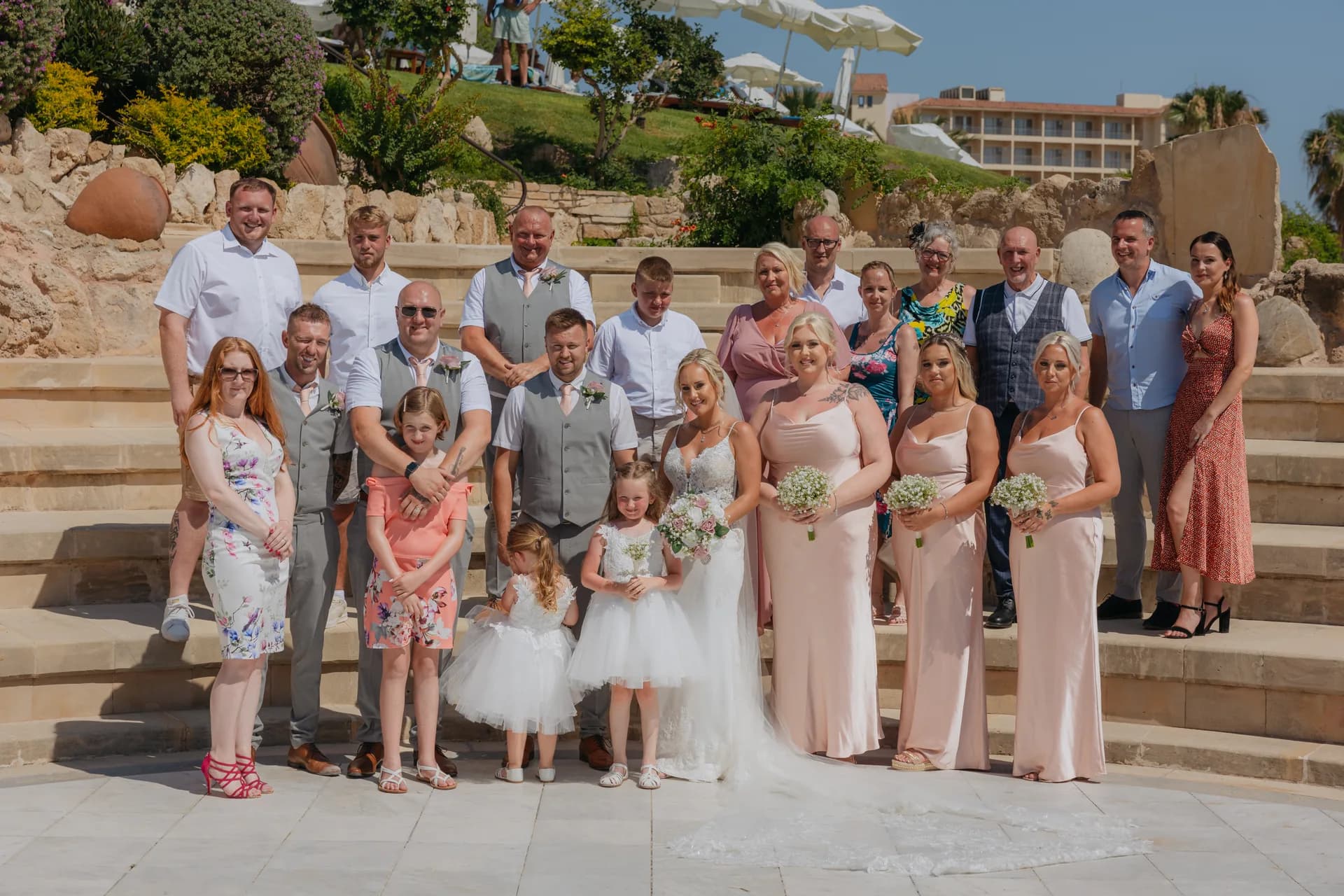 Wedding party gathered on the stone amphitheatre steps at Coral Beach with the hotel rising behind