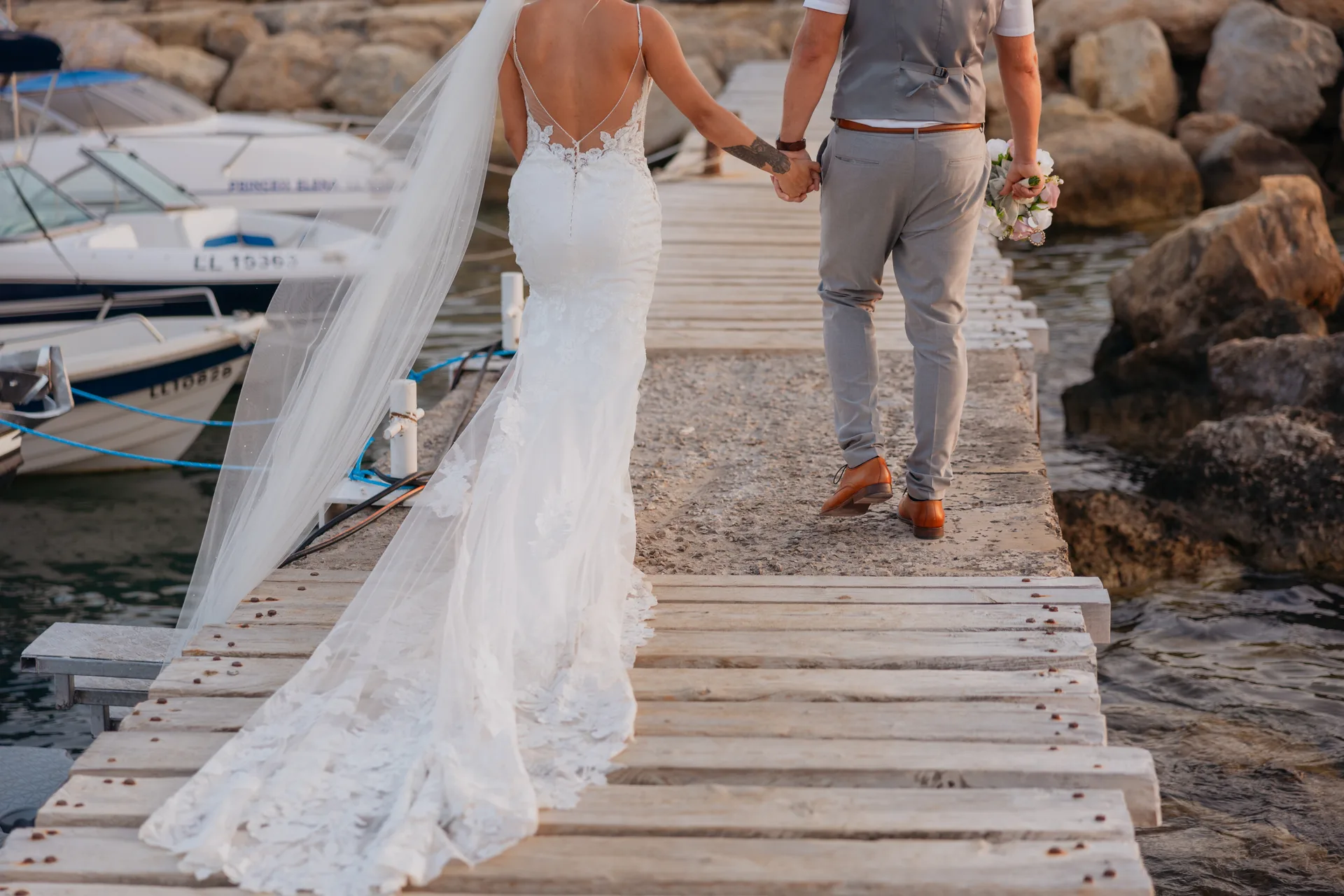 Bride and groom walking the wooden jetty past moored boats at Coral Beach in golden evening light