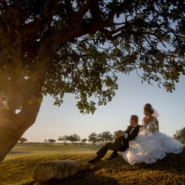 Bride and groom sitting together under a carob tree at sunset in the Cyprus countryside after an intimate wedding ceremony