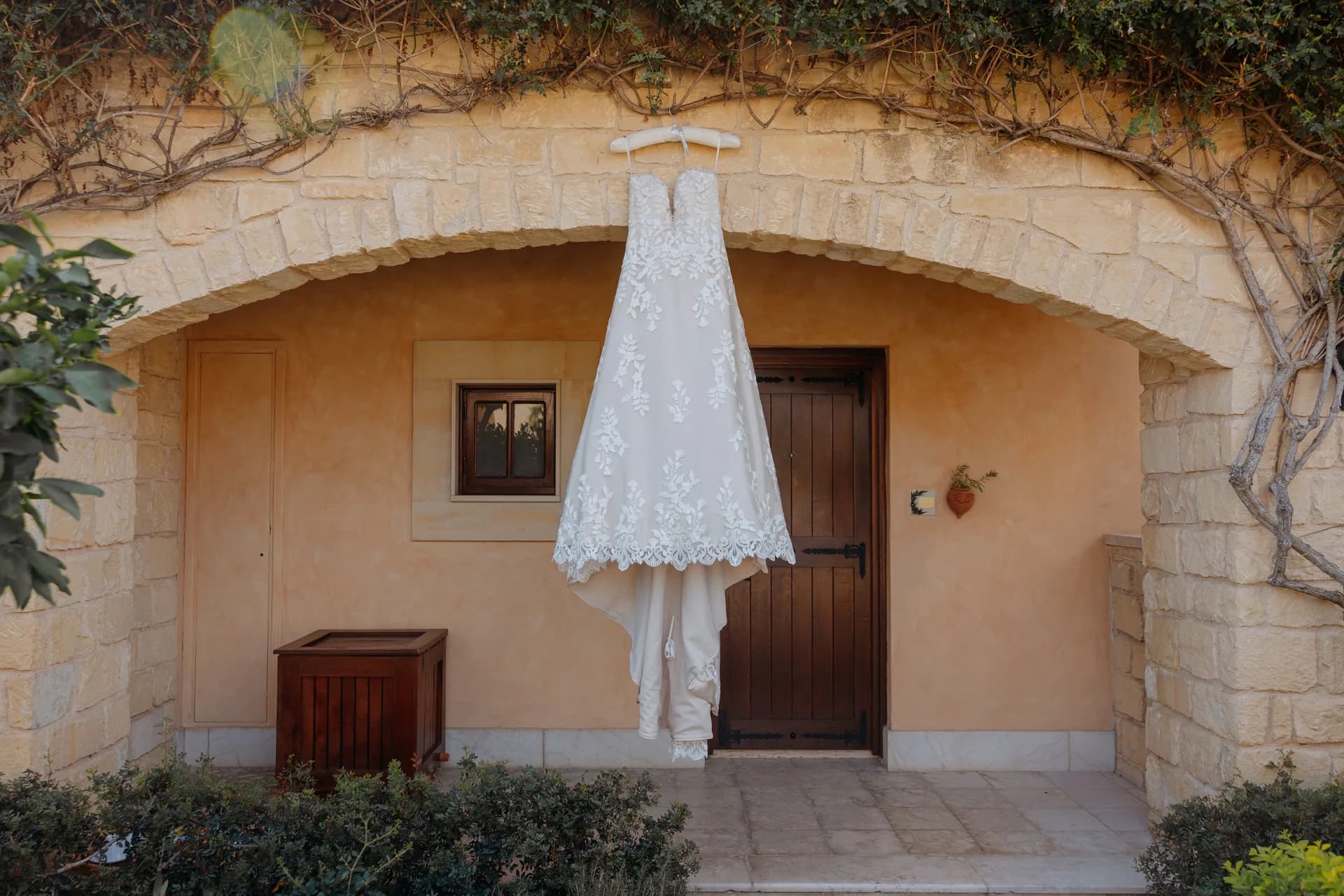 A lace wedding gown hanging in the vine-topped stone arch of an Elysium villa entrance
