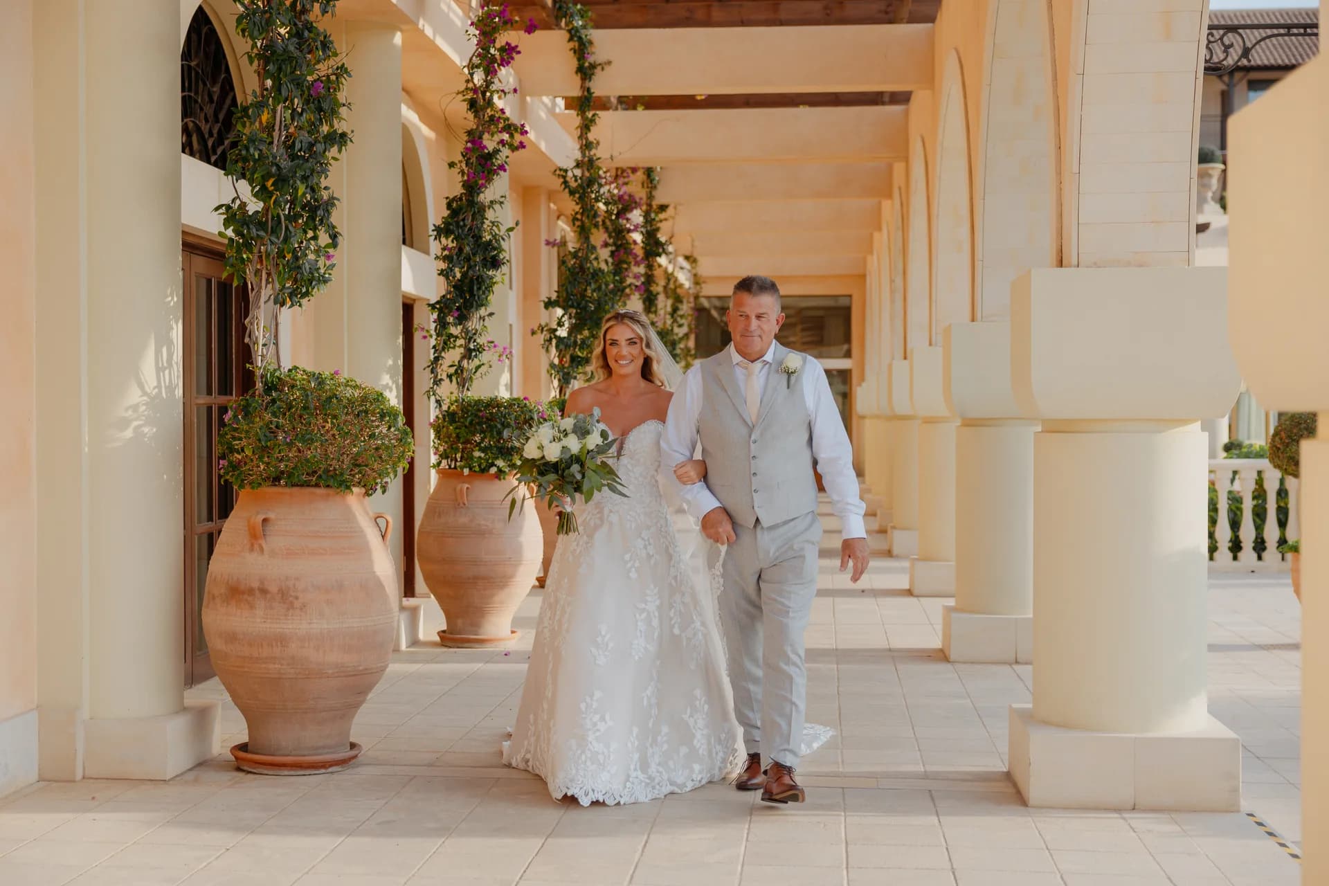 A bride walking the Elysium’s bougainvillea-draped colonnade, lined with giant terracotta urns