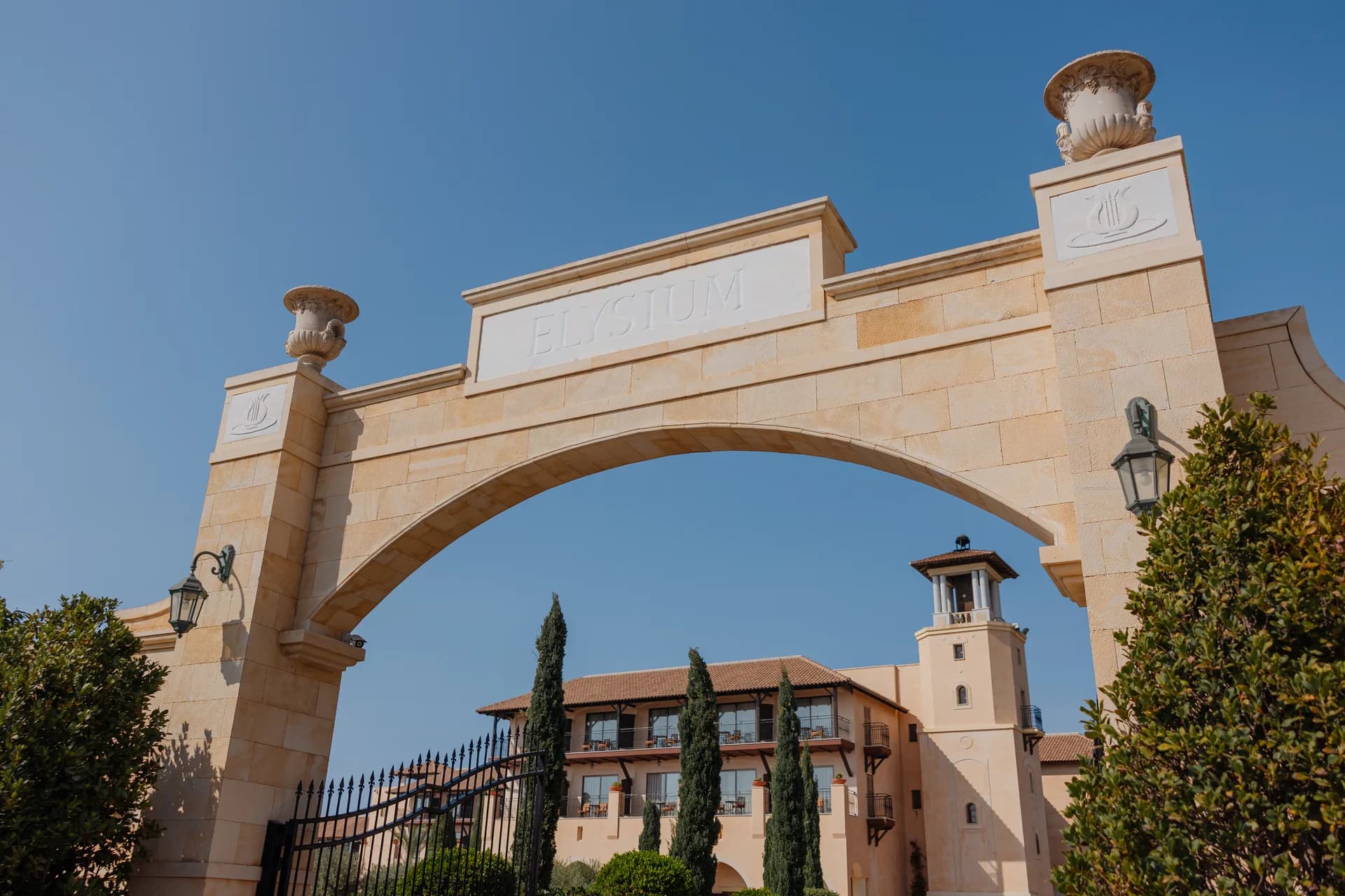 The carved Elysium entrance arch with the hotel’s belvedere tower and cypresses framed beneath a blue sky