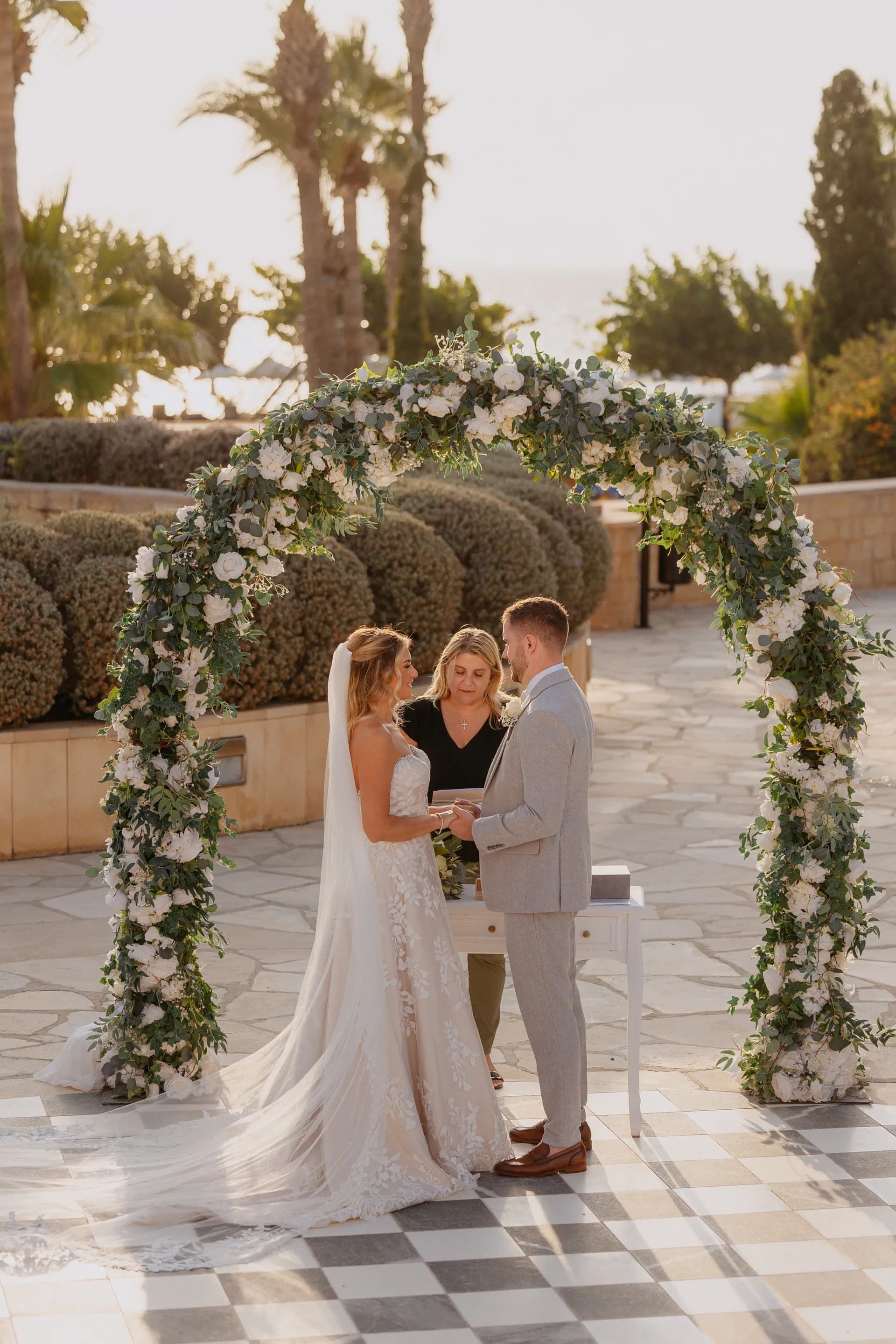 Bride and groom exchange vows beneath the white rose and eucalyptus arch at the Elysium