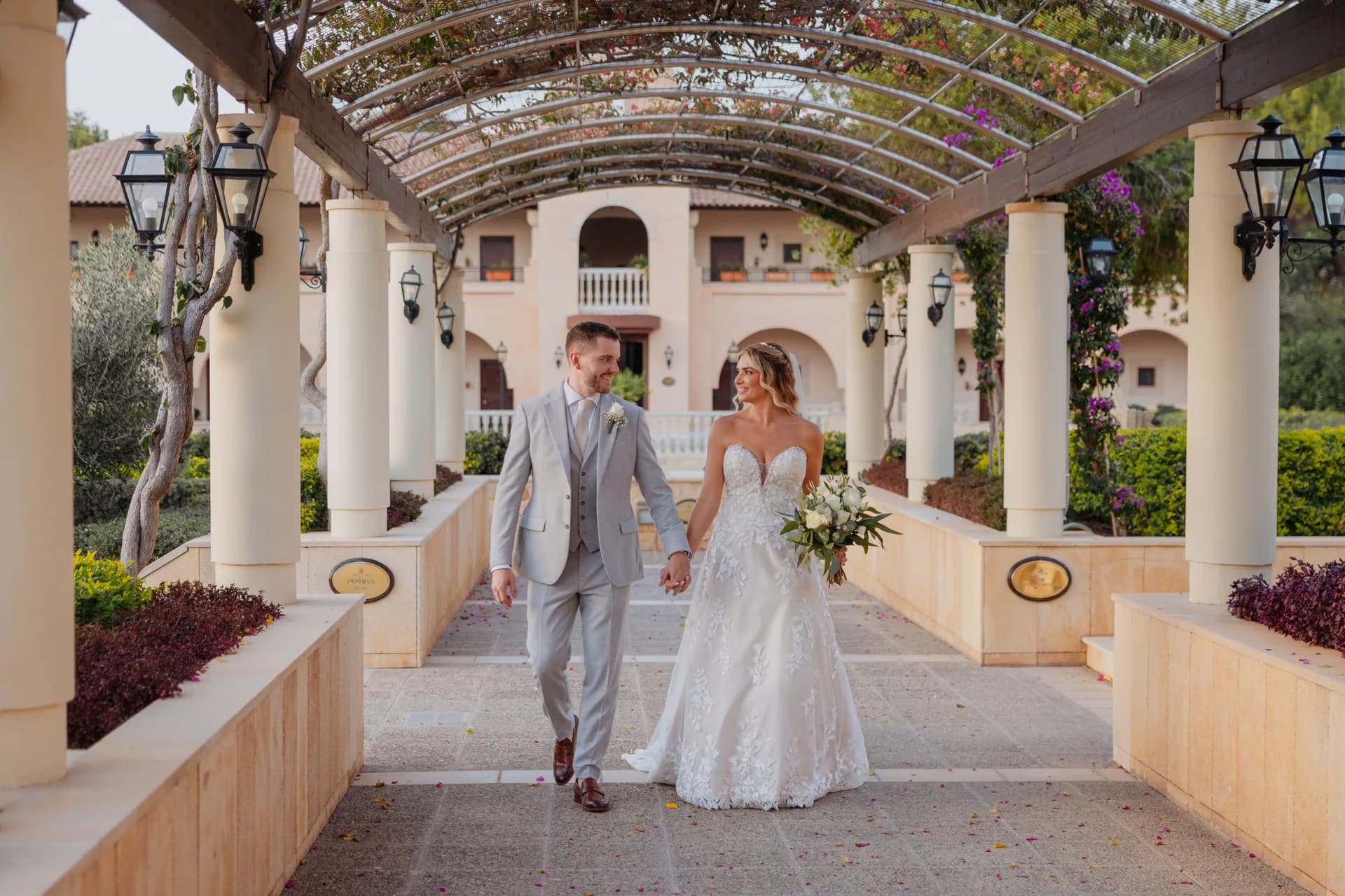 Bride and groom beneath the Elysium’s vine-covered pergola walkway, columns and lanterns receding behind