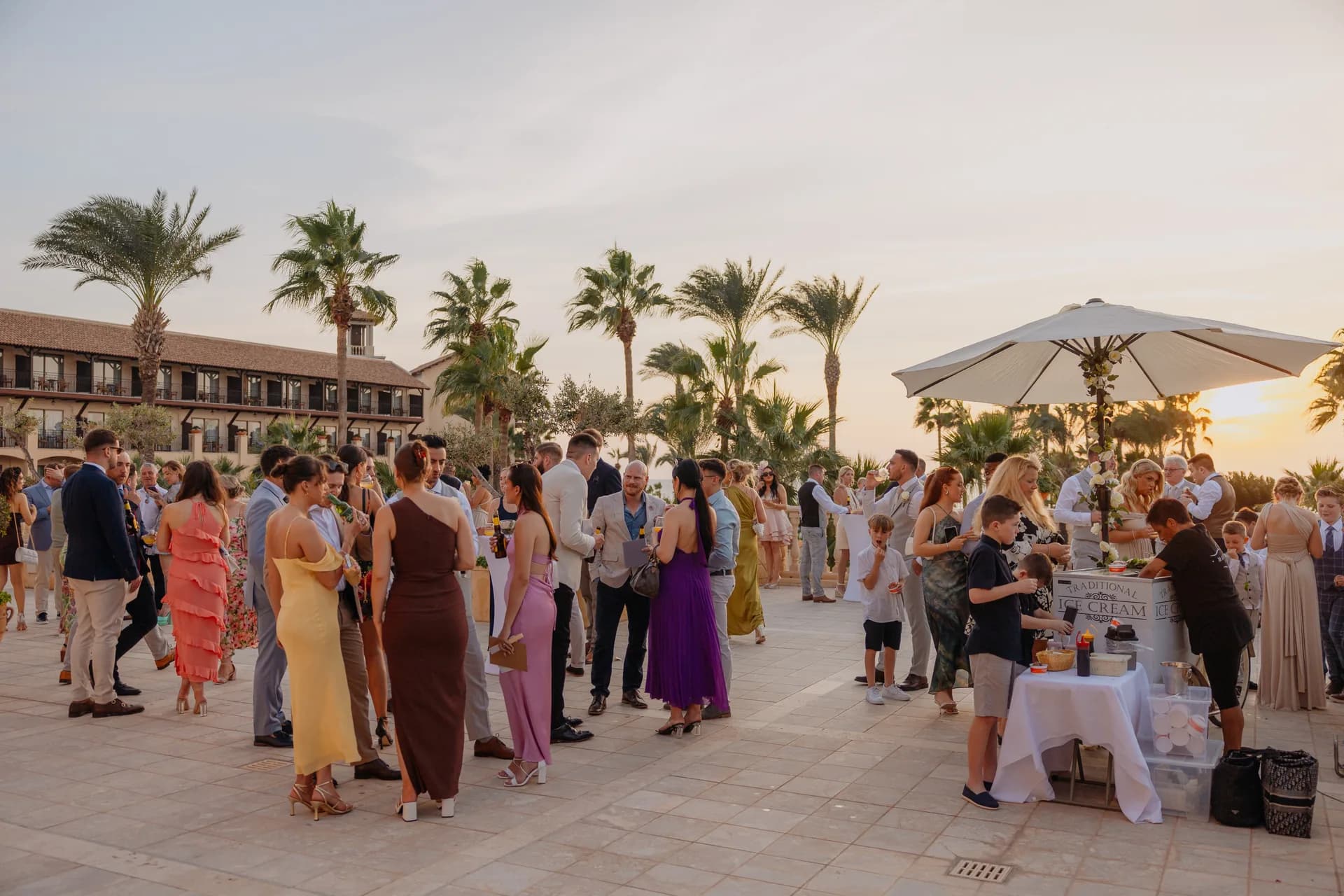 Guests at a drinks reception on the Elysium’s palm-fringed terrace at sunset, the hotel wing glowing behind