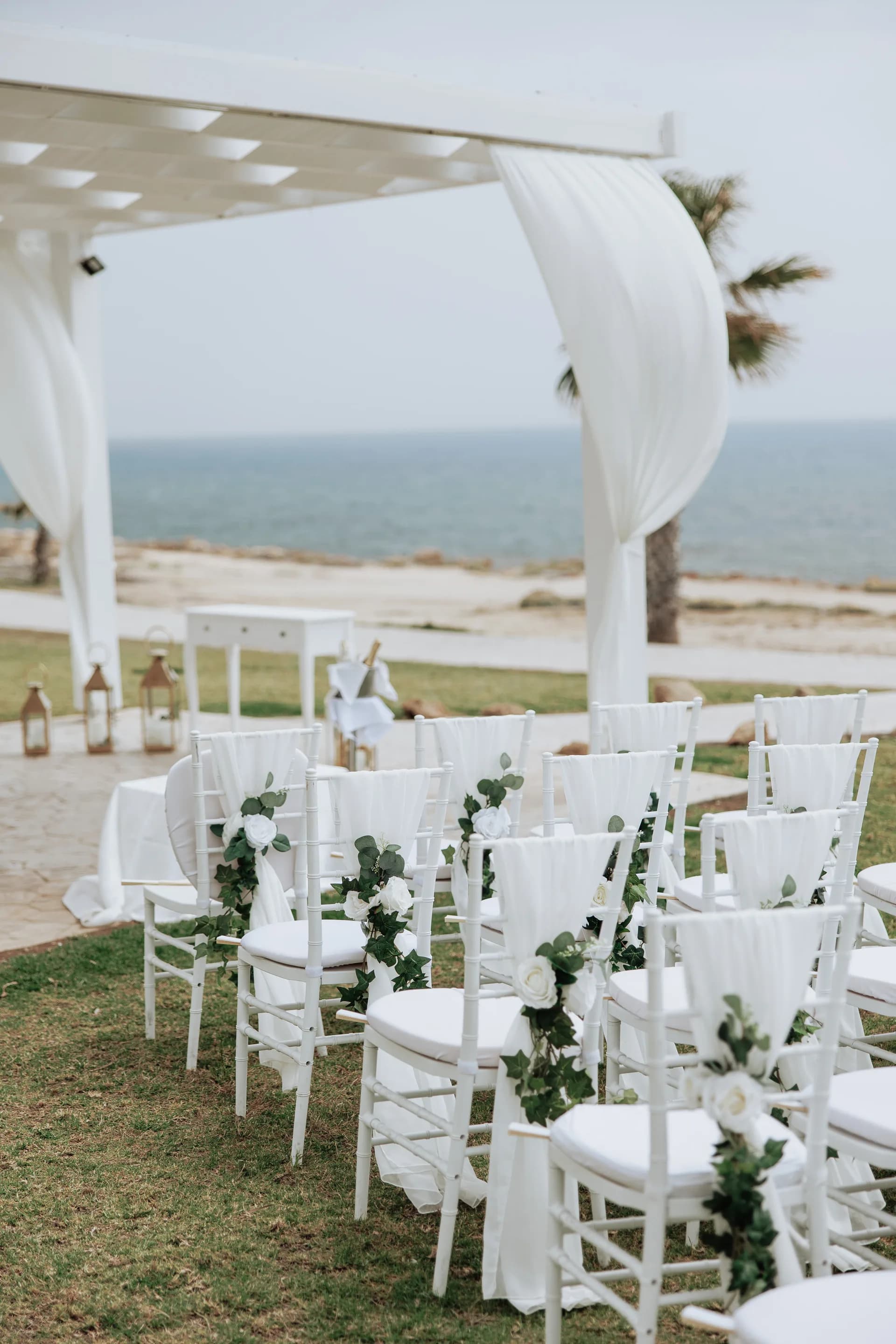 White chiavari chairs dressed with roses and ivy facing the sea at King Evelthon’s ceremony lawn