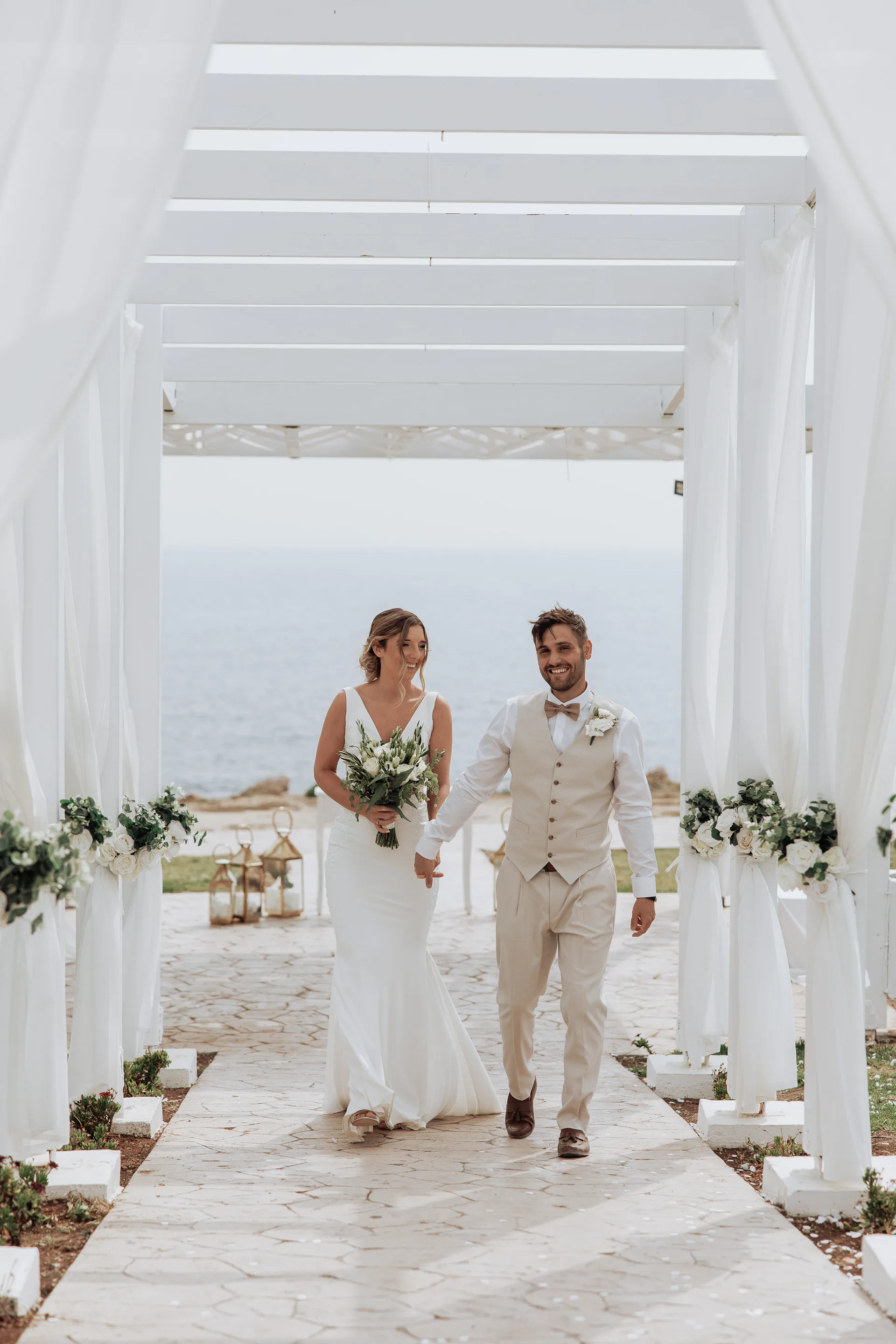 Newlyweds walking out of King Evelthon’s draped white colonnade, sea framed behind them