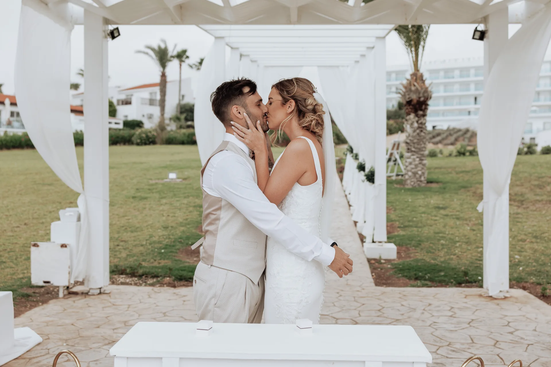 First kiss under King Evelthon’s draped pergola, with lawns, palms and the white resort facade behind