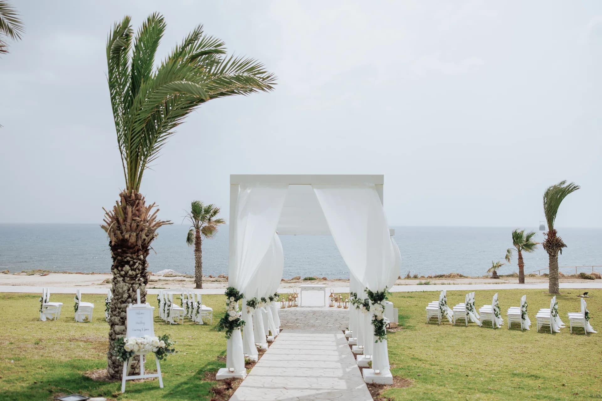 King Evelthon’s seafront lawn set for a ceremony: draped arch, white chairs, palm and open sea