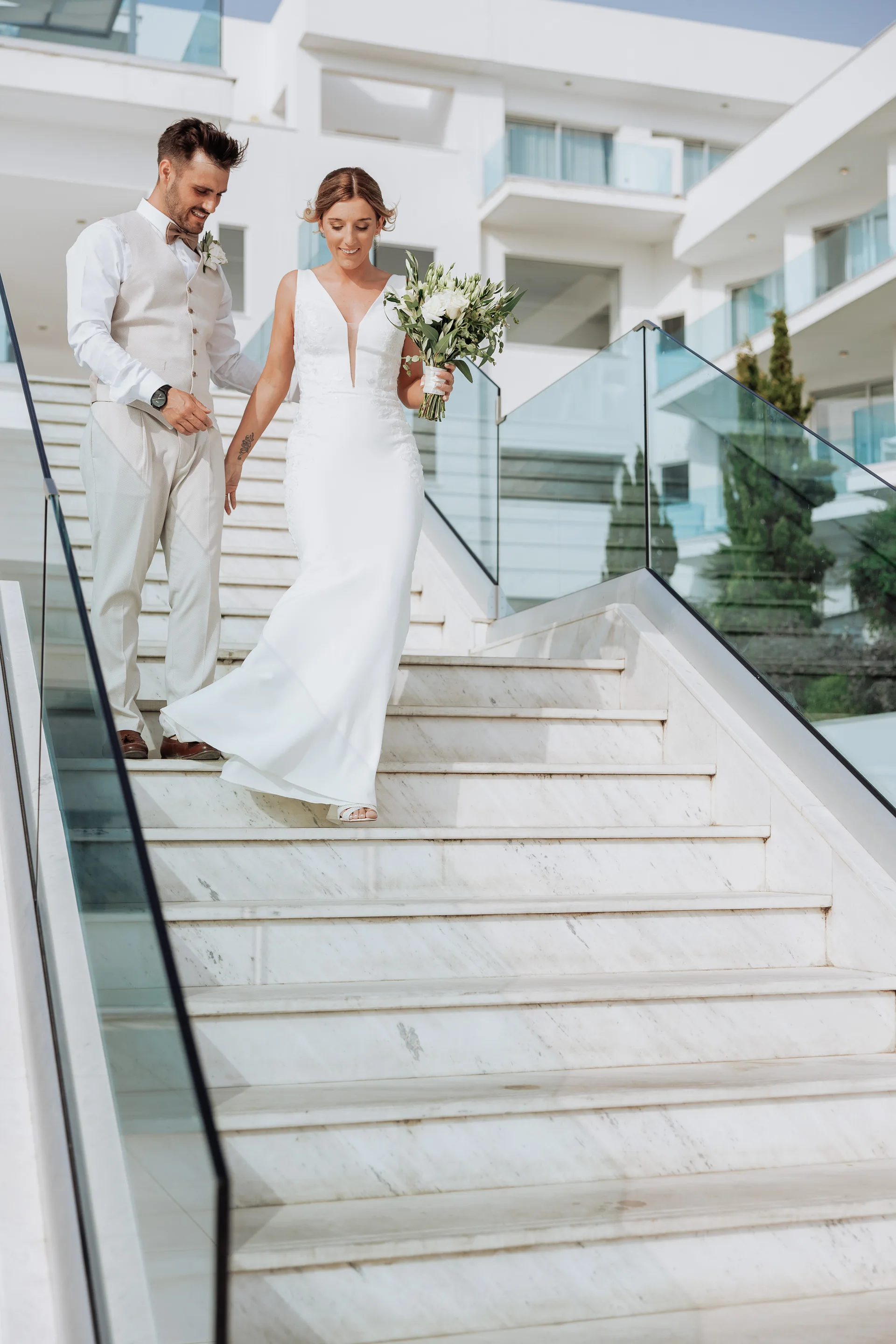 Bride and groom descending King Evelthon’s wide marble staircase between glass balustrades