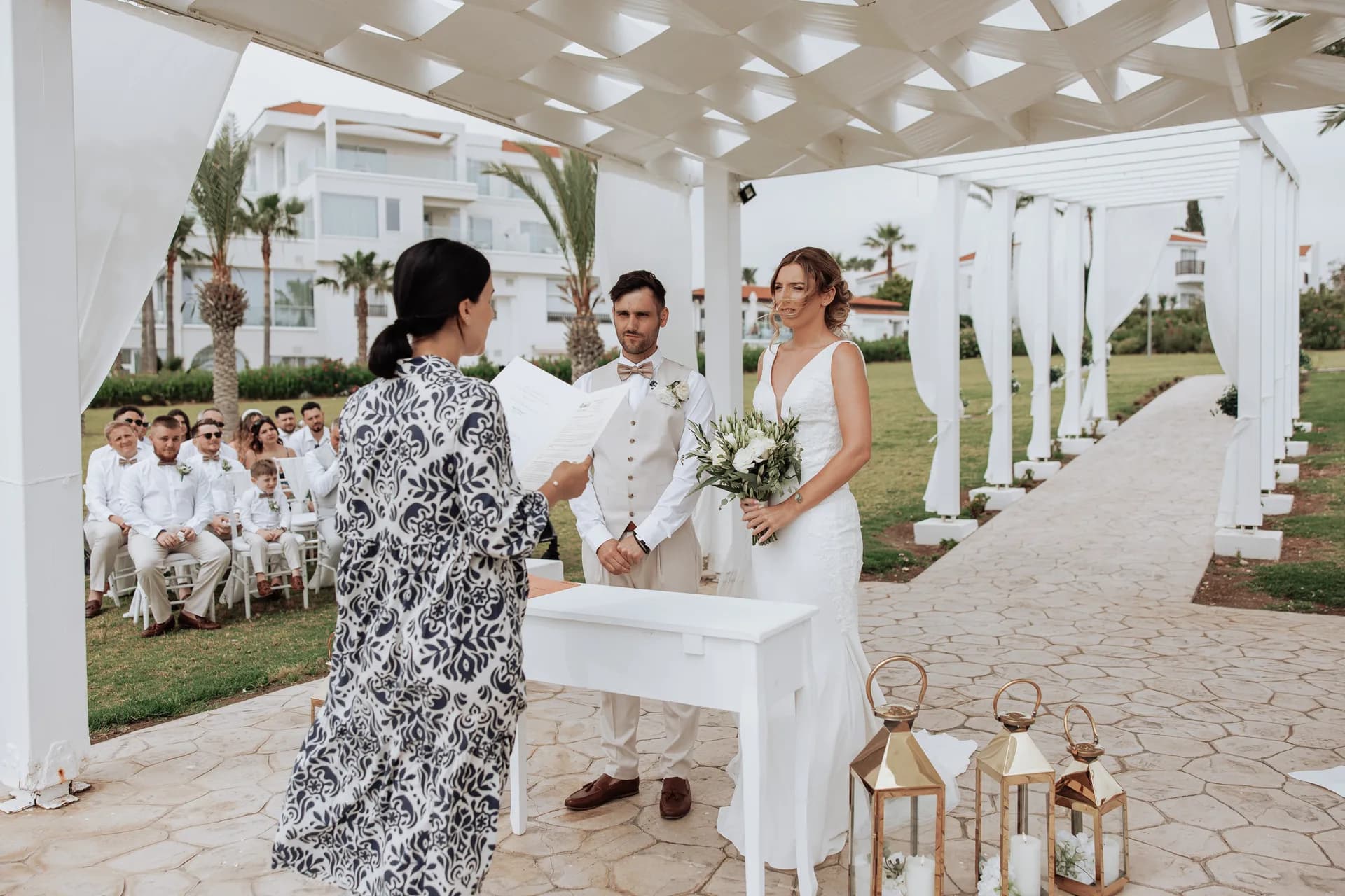 A ceremony under King Evelthon’s beachfront pergola, guests seated on the lawn behind