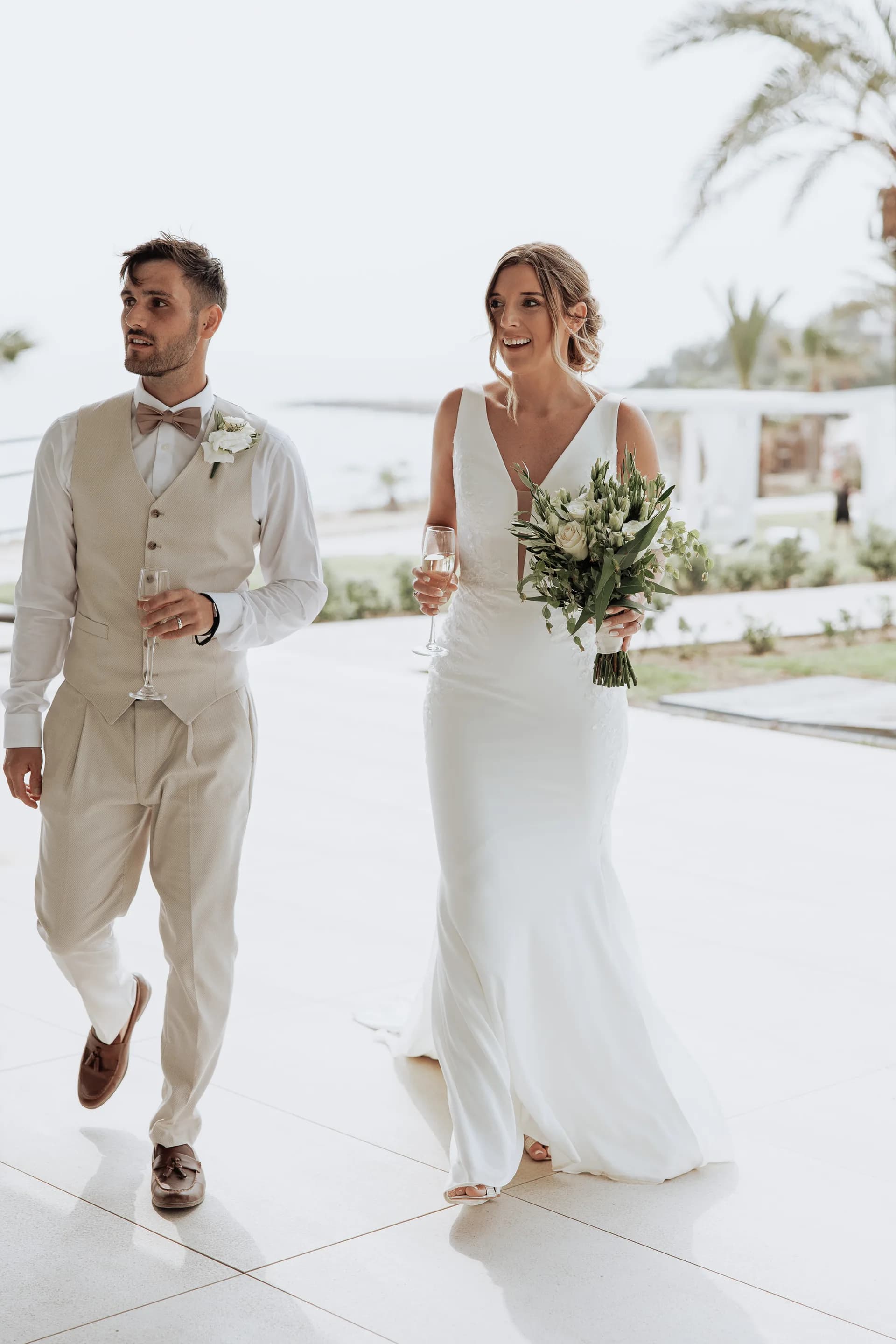 Bride and groom crossing the white pool terrace at King Evelthon, palms overhead and the sea beyond