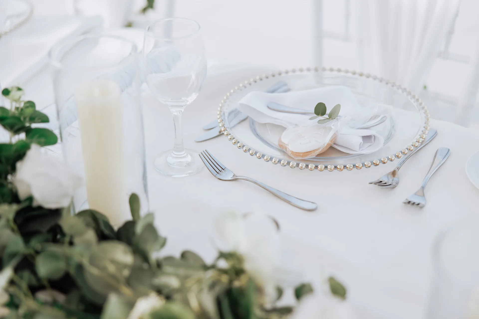 Beaded charger, pillar candles and trailing eucalyptus dressing a King Evelthon wedding table