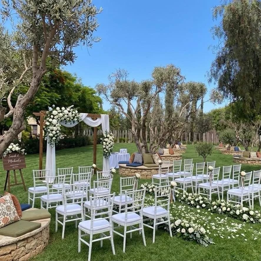 Illustrative garden ceremony design with a floral arch, white chairs and olive trees
