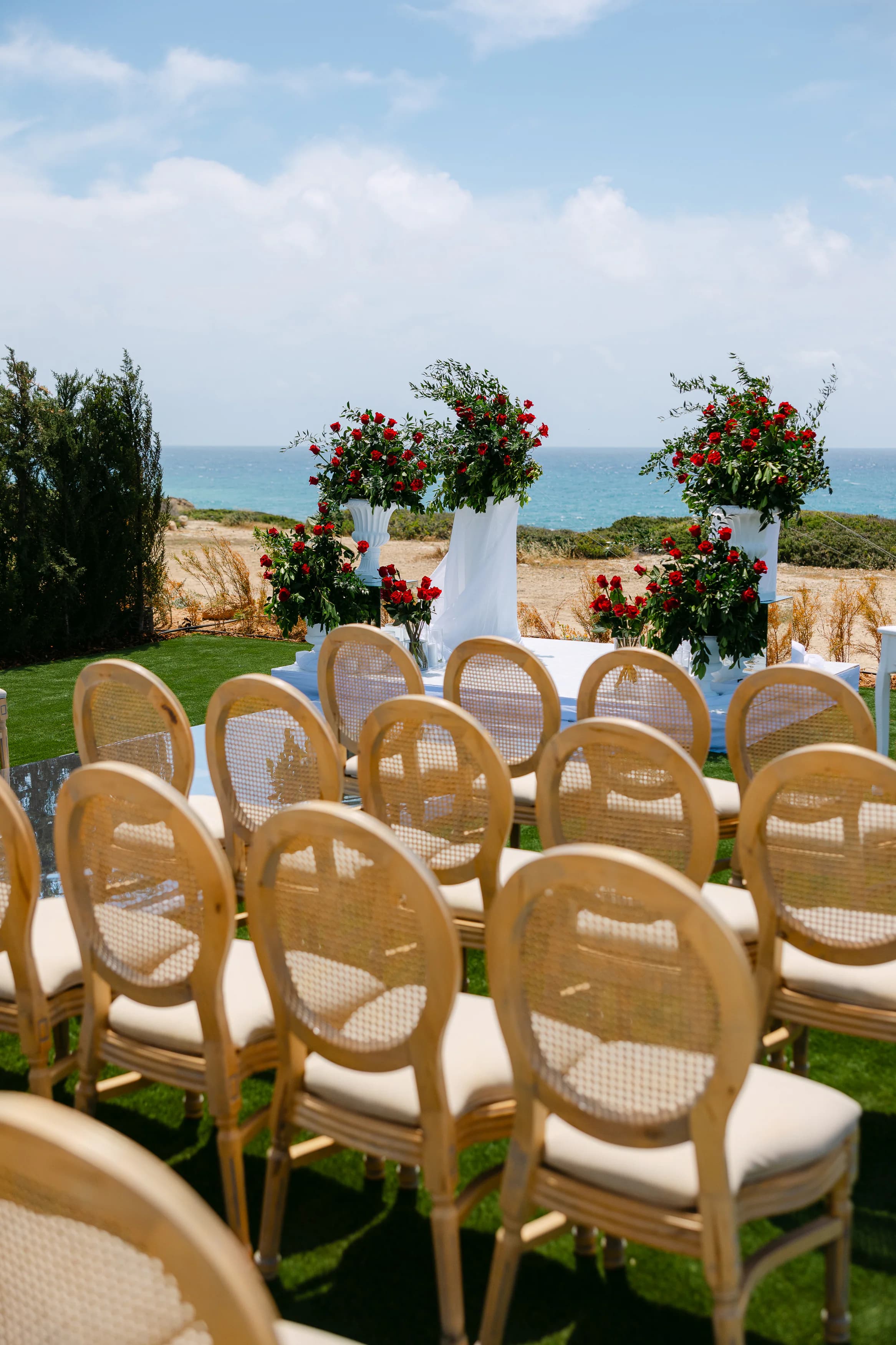 OZEA ceremony altar with twin tall red rose arrangements on white plinths against the Sea Caves Paphos coastline