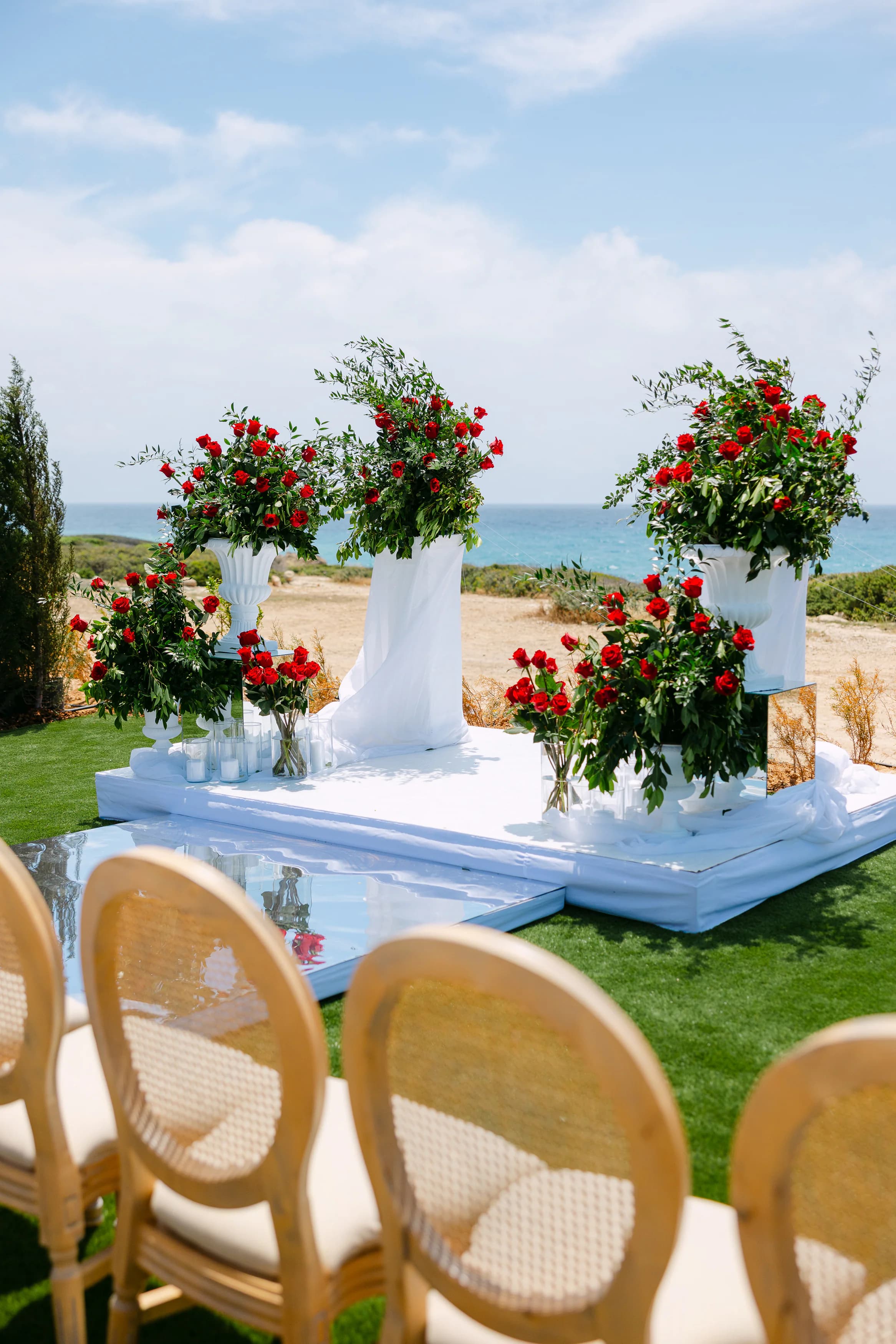 Close-up of the OZEA wedding altar — twin tall red rose arrangements on white plinths with trailing greenery