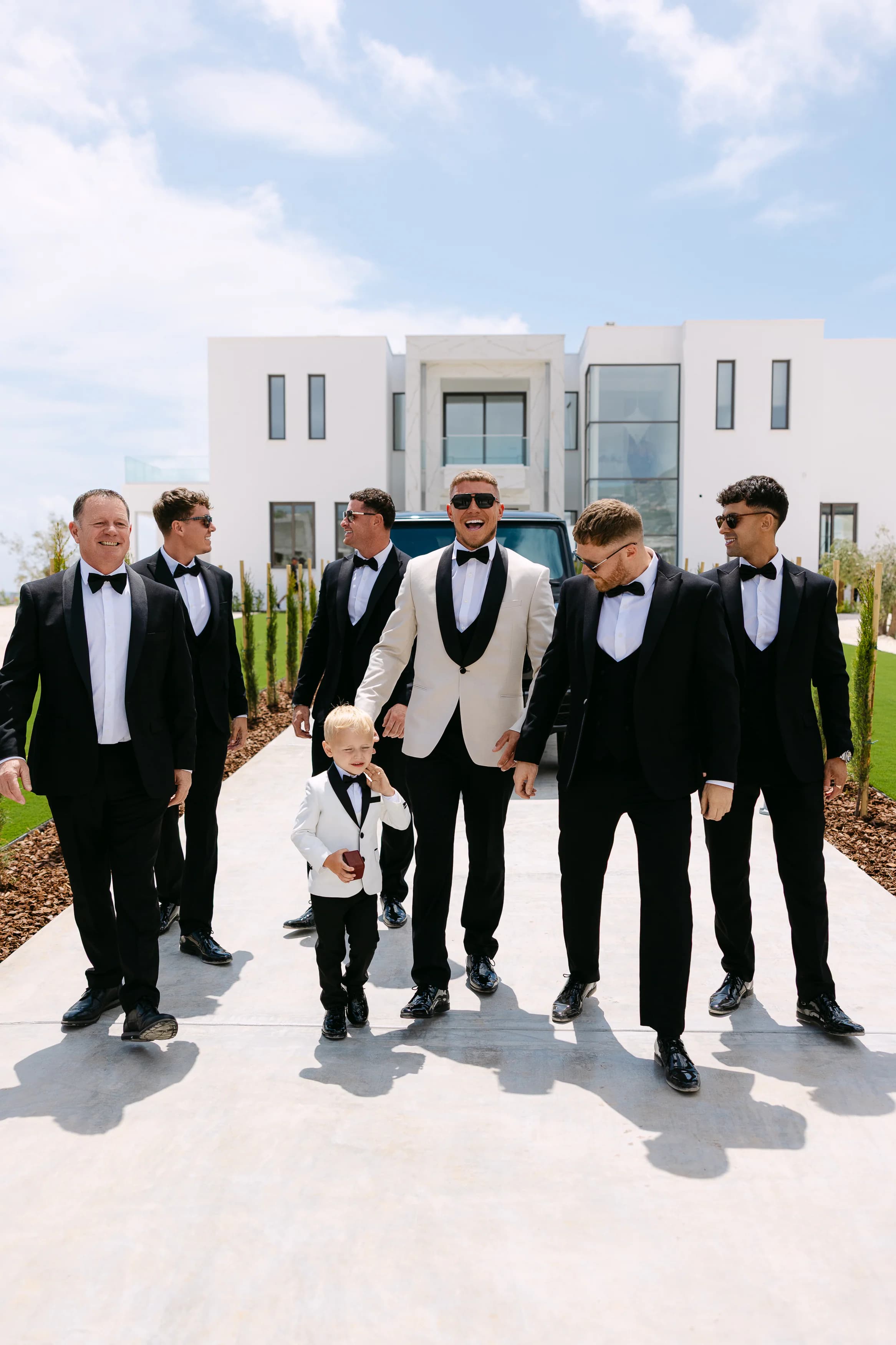 Groom and groomsmen walking together toward the OZEA wedding ceremony with a pageboy at the front