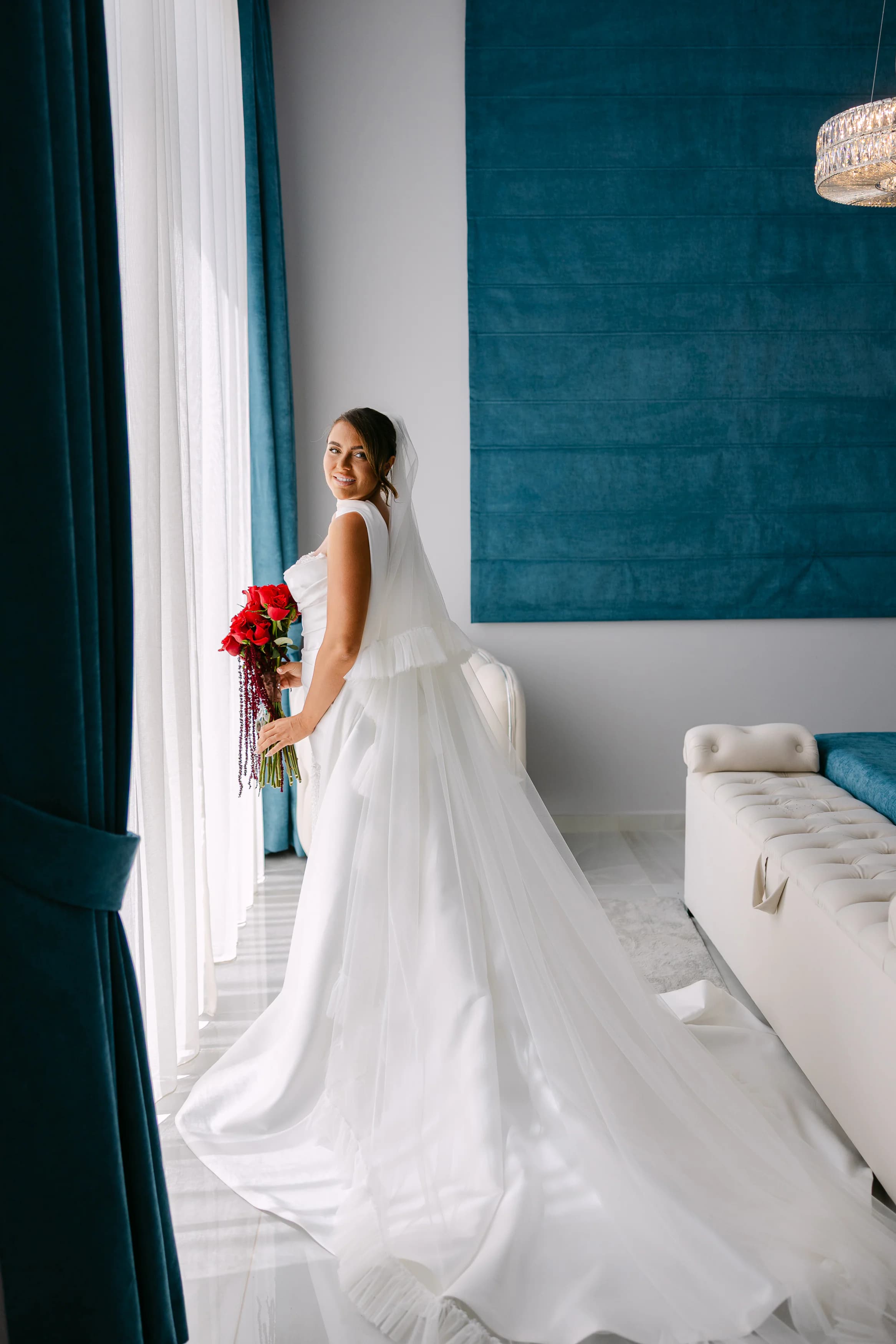 Bride Abbie in a flowing white ballgown holding a crimson rose bouquet inside the OZEA bridal suite, Sea Caves Paphos