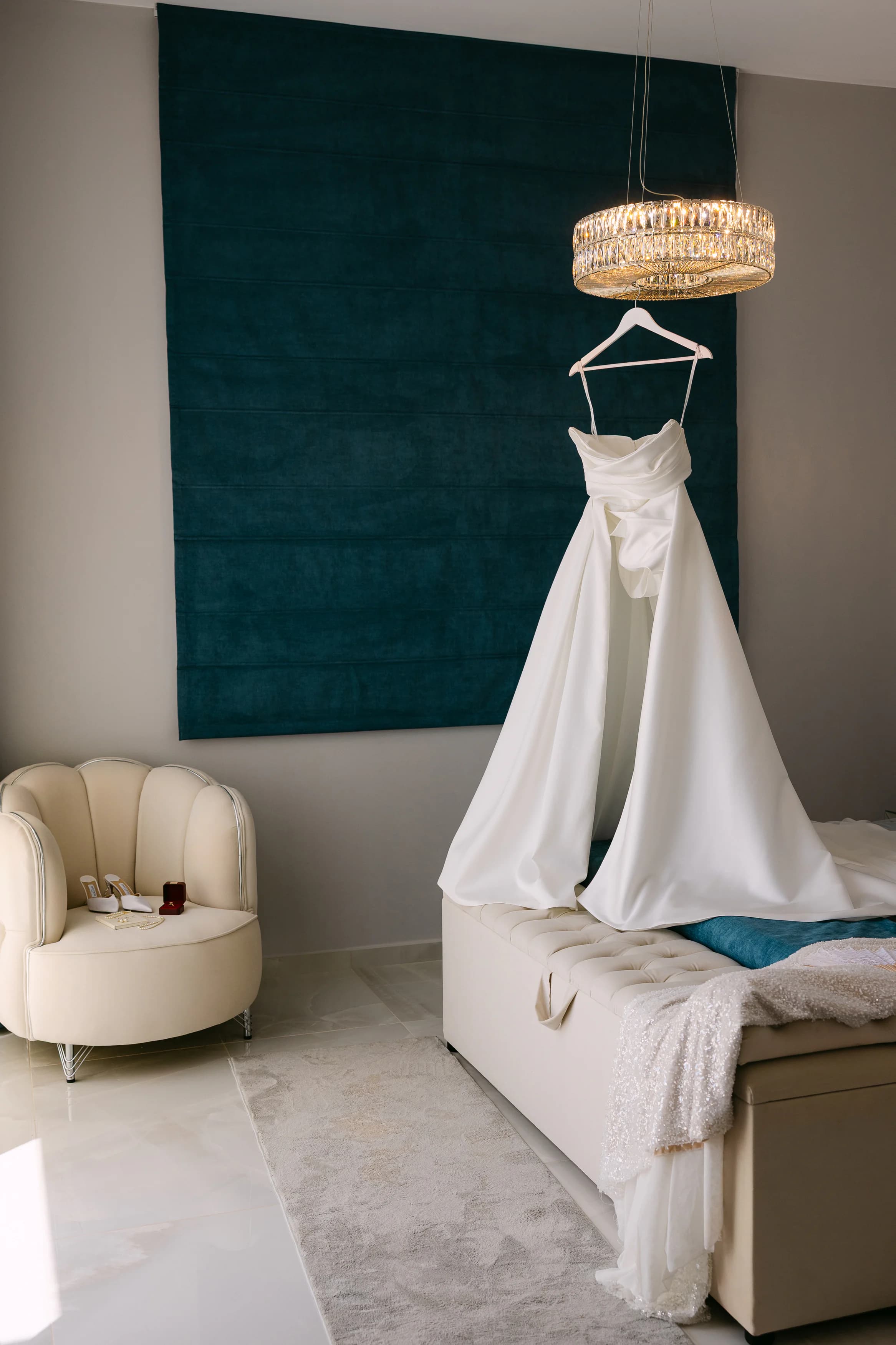 Bride's white wedding gown hanging in the OZEA bridal suite against a deep teal velvet wall with crystal chandelier overhead
