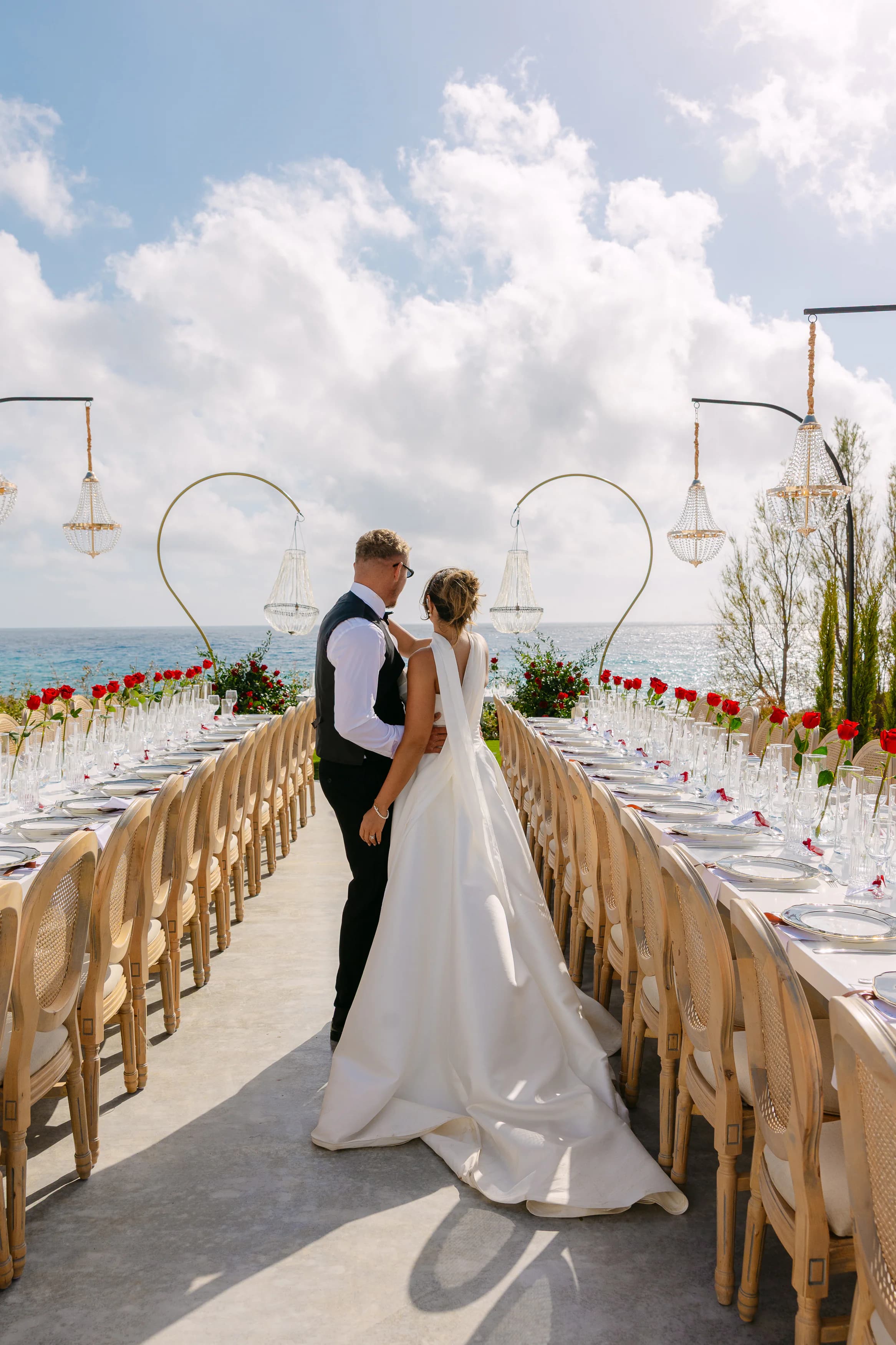 Bride and groom standing at the end of the OZEA reception table looking out over the Sea Caves Paphos coastline