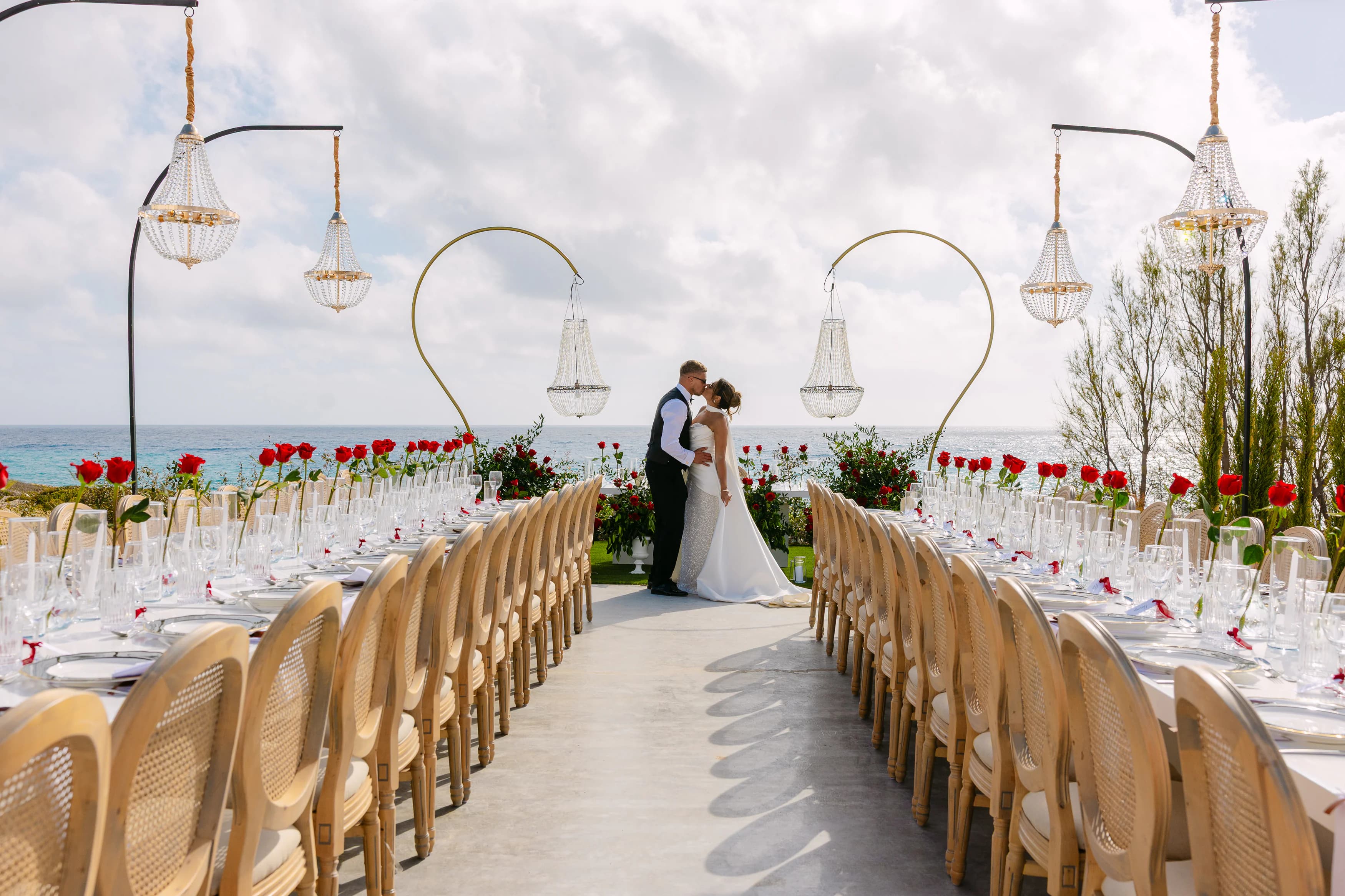 Bride and groom kissing between OZEA's signature gold heart arches and crystal chandeliers above the long reception table