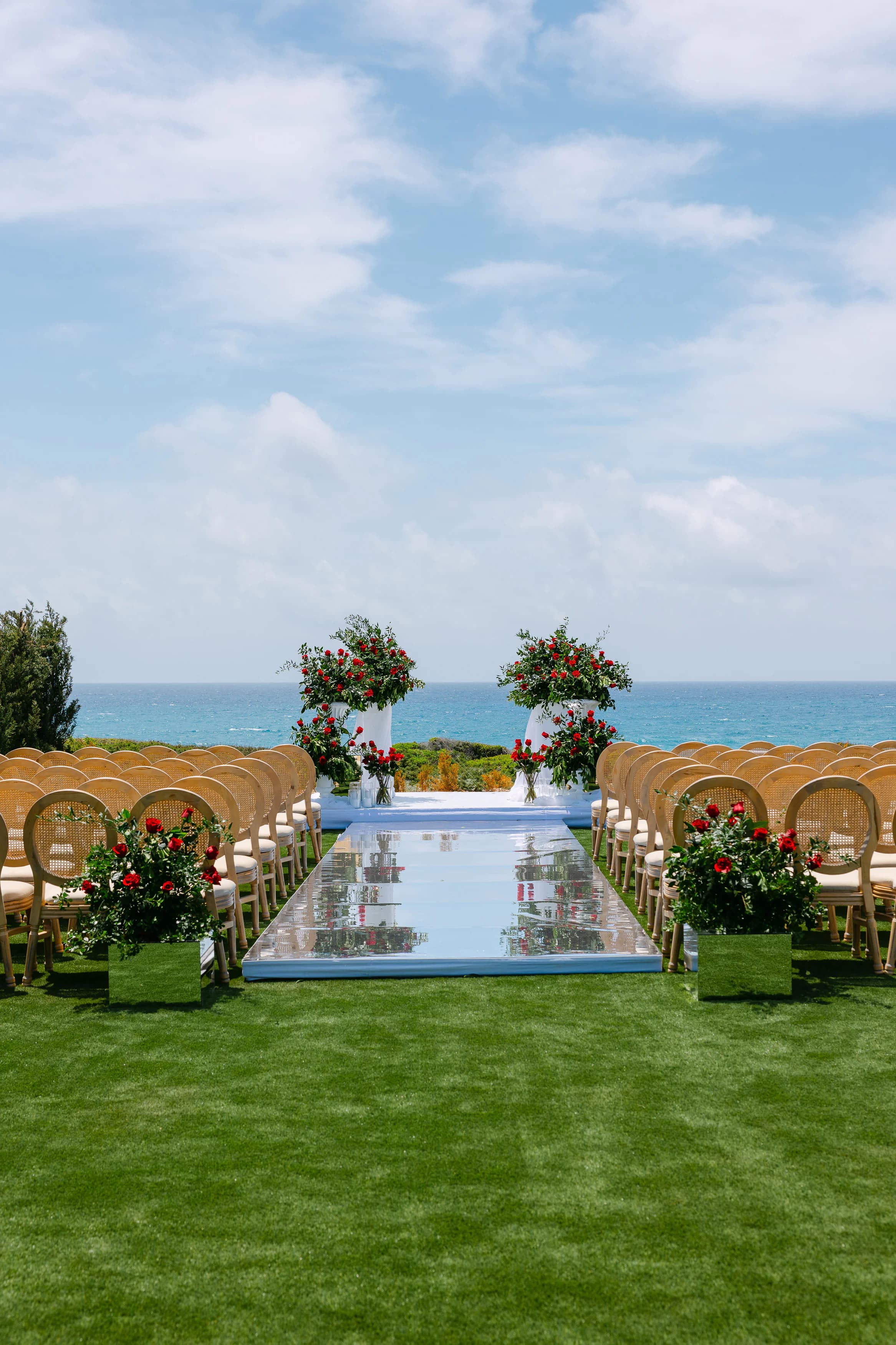 Mirrored ceremony aisle with red rose pedestals at OZEA, Sea Caves Paphos — vertical view from the back of the aisle
