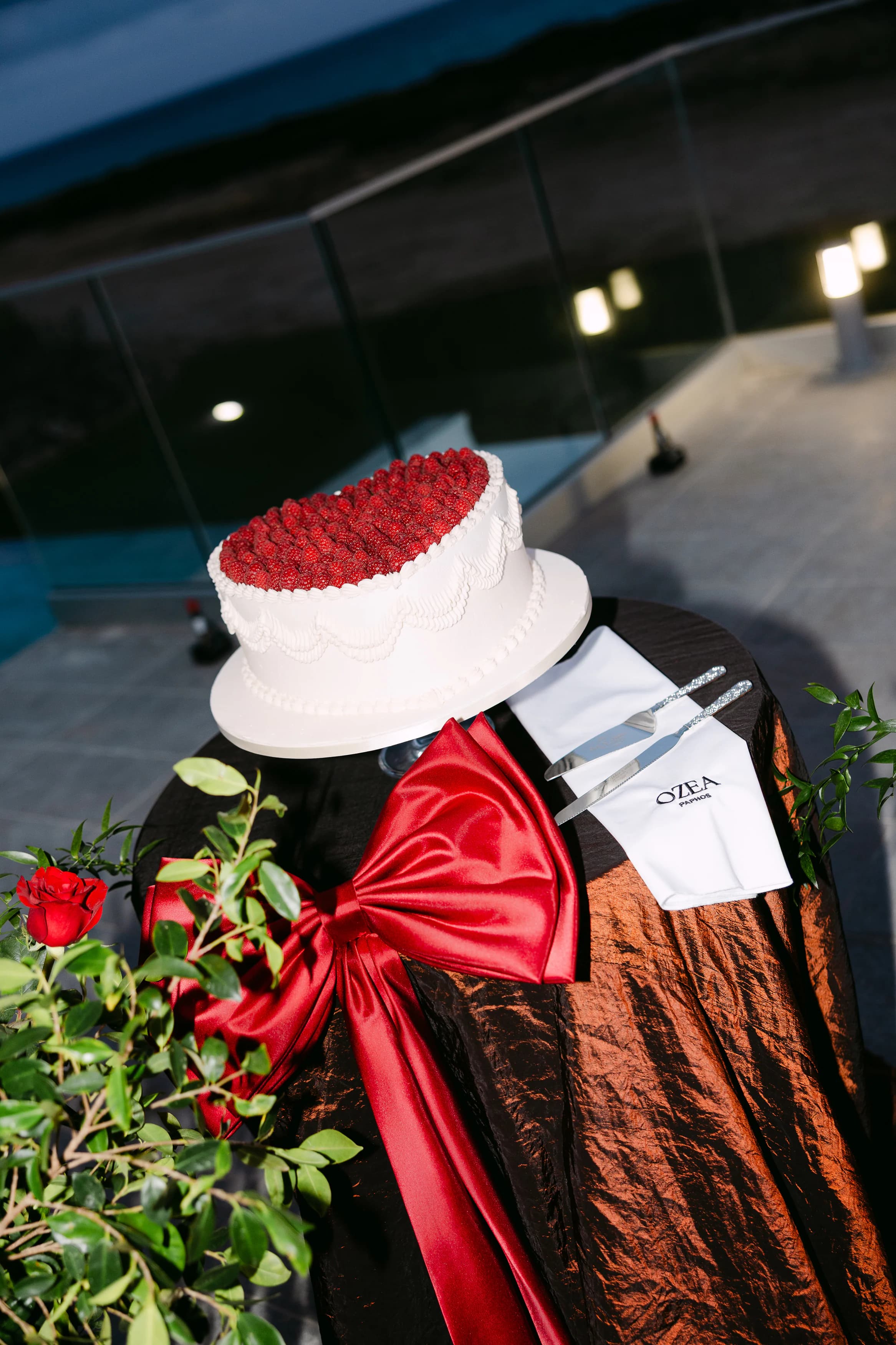 Crimson rosette wedding cake on a mocha velvet table with a red satin bow at OZEA Sea Caves Paphos