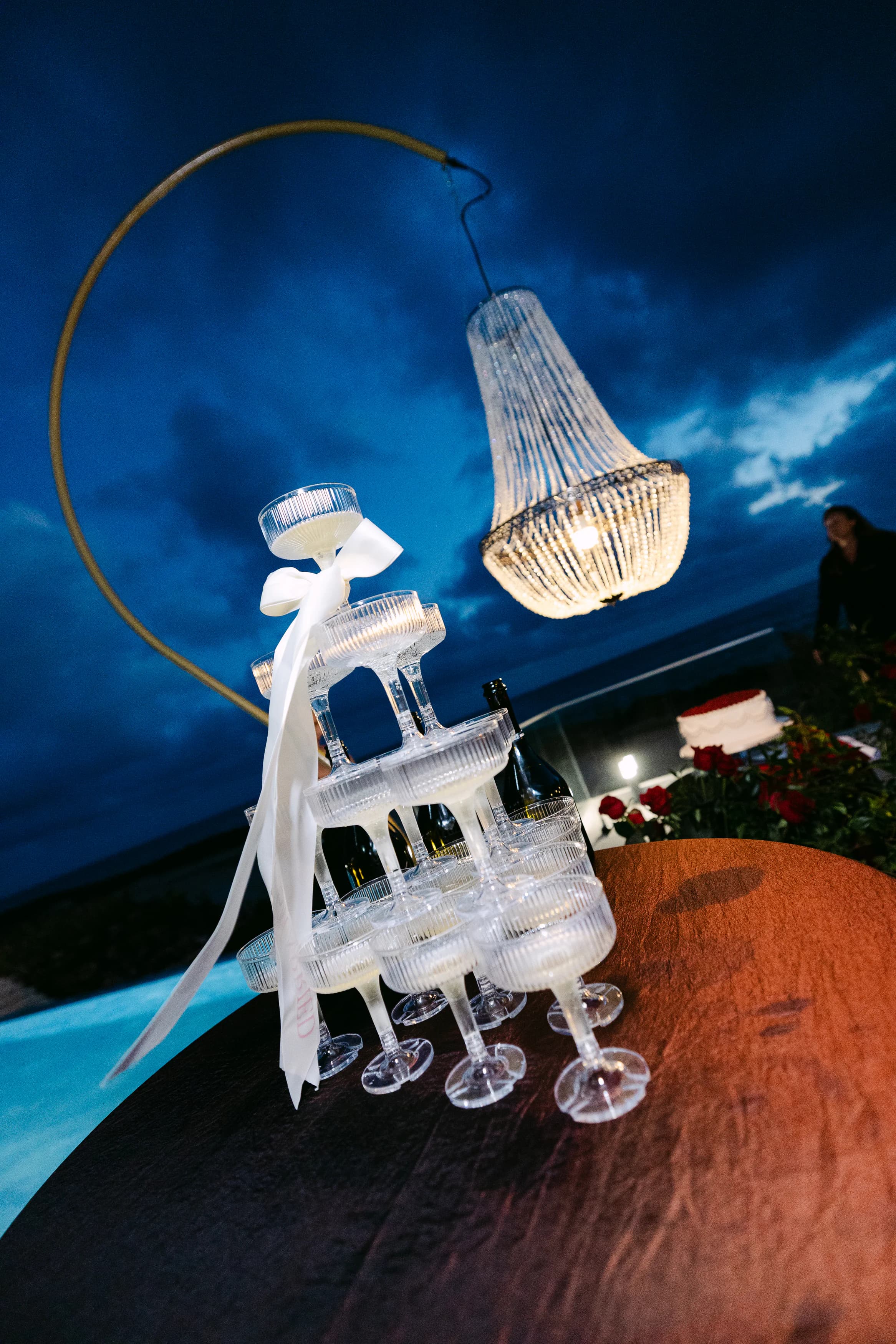 Four-tier champagne tower beneath a crystal chandelier at twilight on the OZEA terrace, Sea Caves Paphos