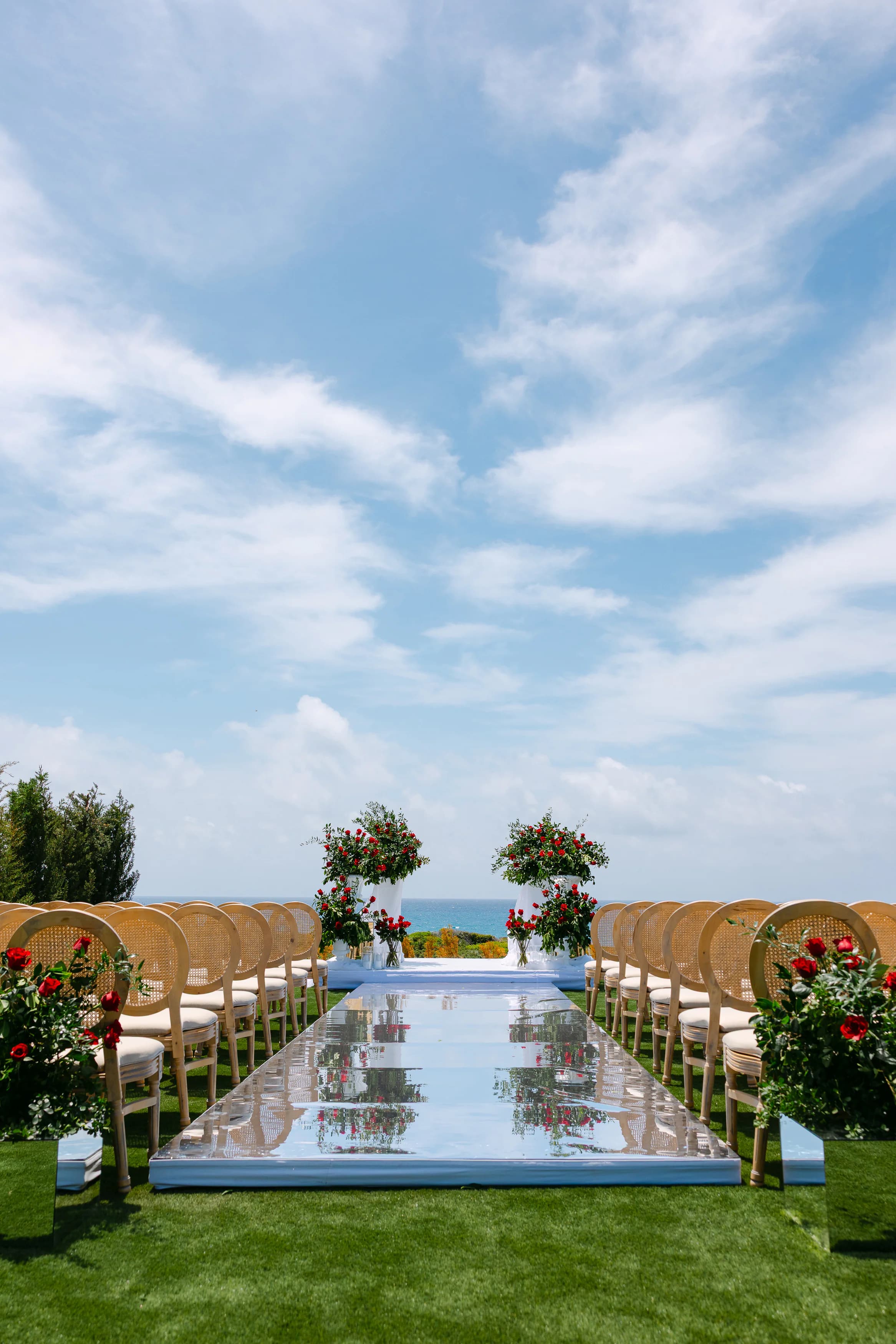 Vertical view of the OZEA ceremony aisle at midday with sky-heavy framing and red rose altar arrangements