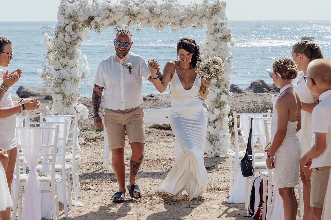 Couple walking beneath a ceremony arch at Faros Lighthouse Beach
