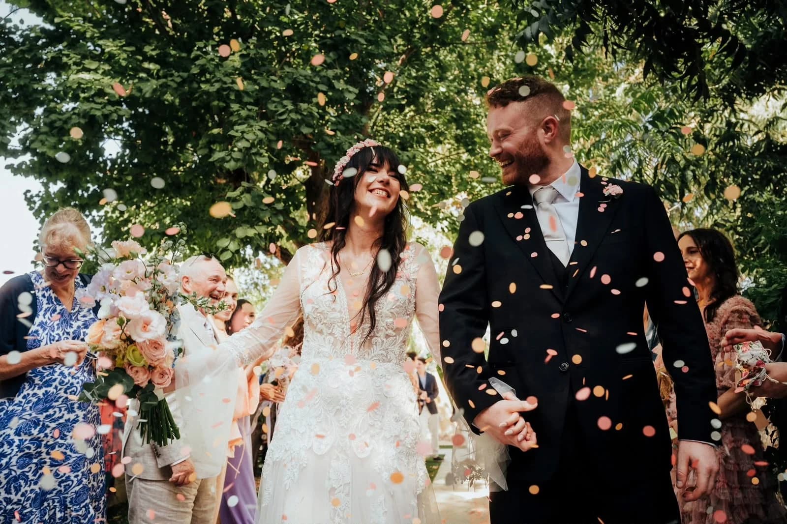 Newlyweds walking hand in hand through confetti with wedding guests at Vasilias