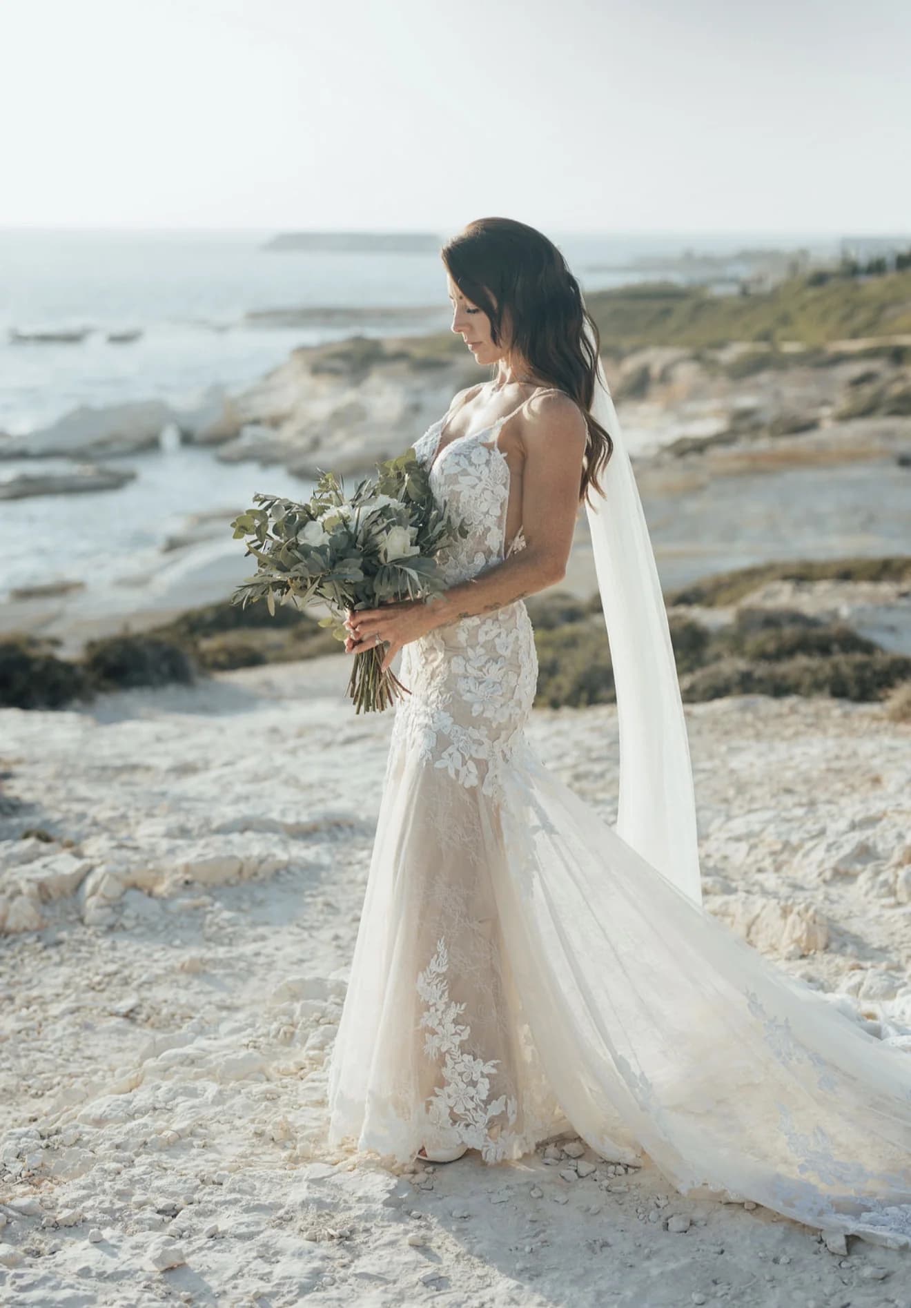 Bride standing alone on the rocky coast with the sea behind her