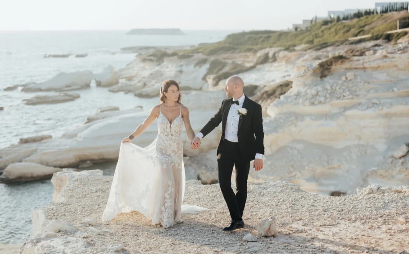 Newlyweds walking hand in hand along the white rocky shoreline
