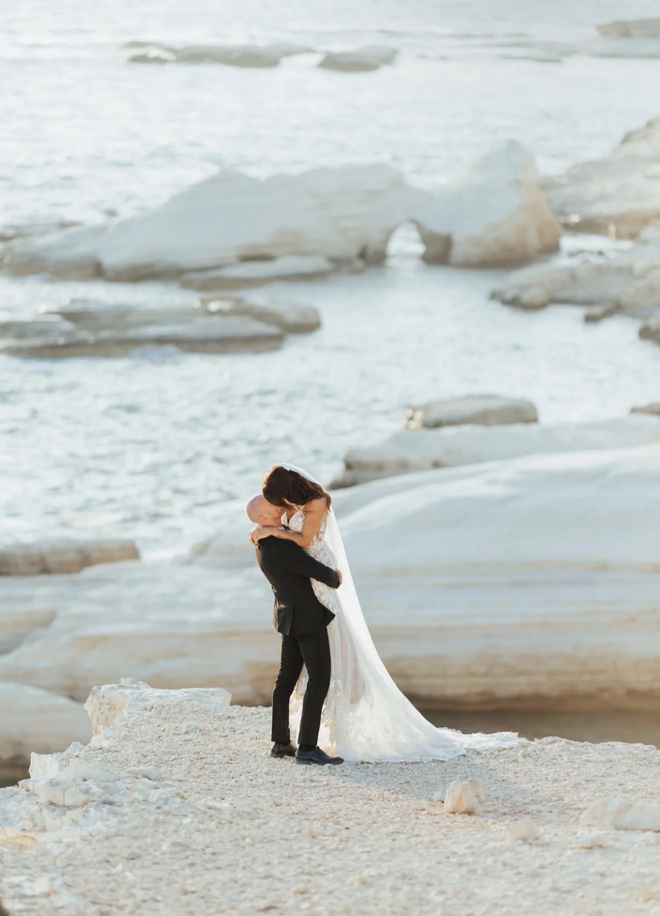 Newlyweds embracing beside the pale limestone shore